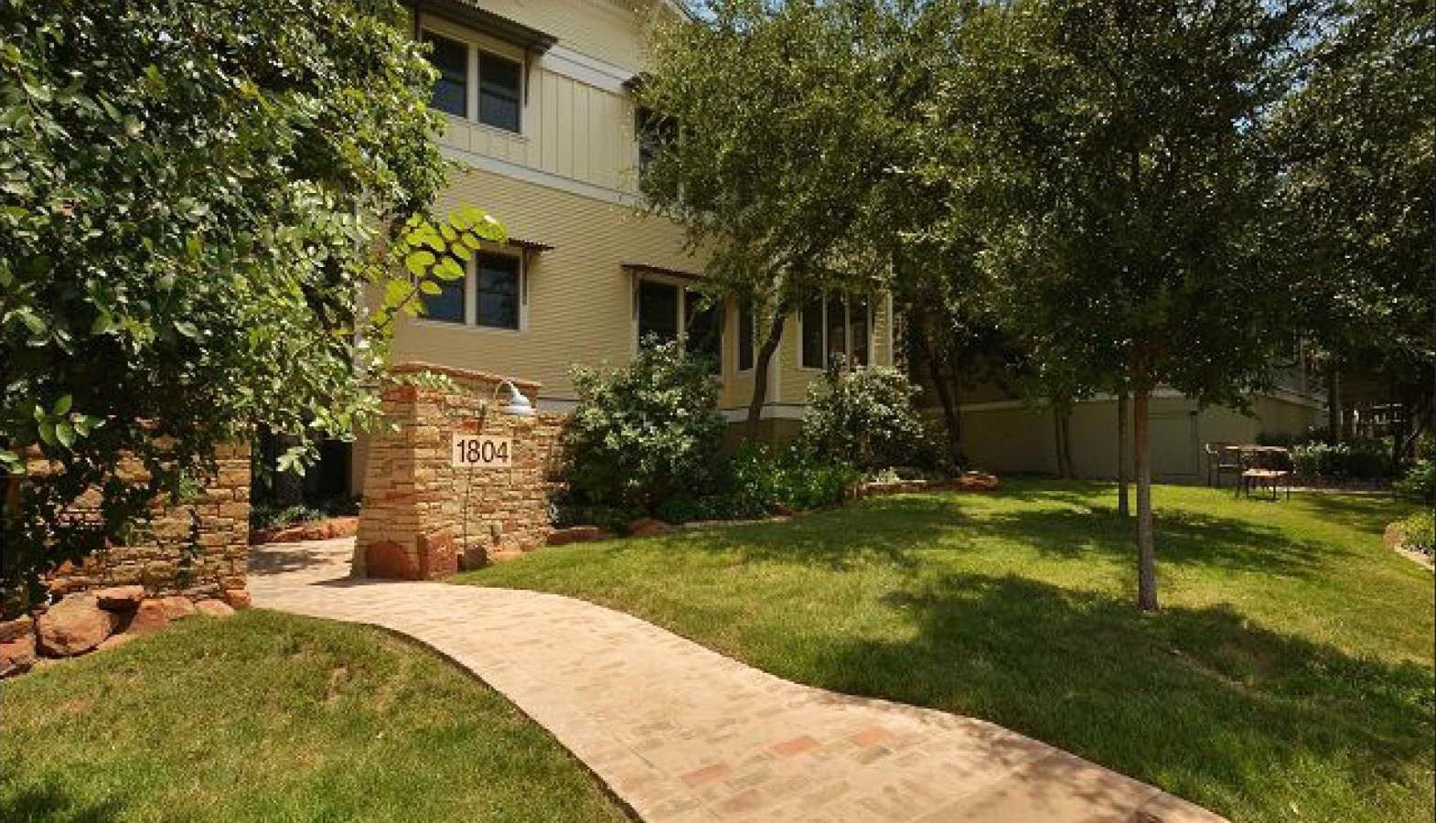 Stone path leading to a two-story building with a light yellow exterior, surrounded by trees and green grass.