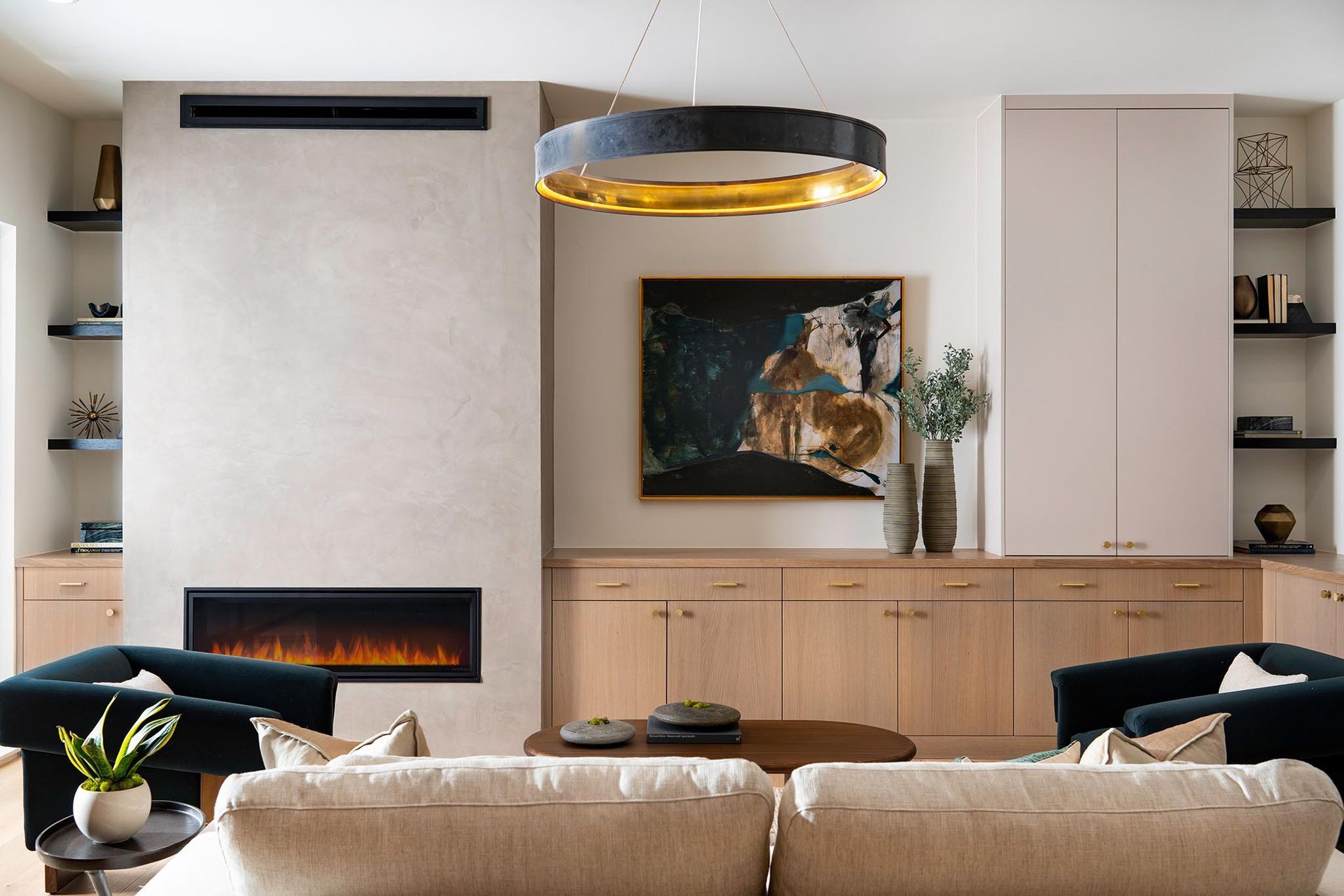 Living room with fireplace, built-in storage, and modern artwork. Features beige sofa and dark armchairs.