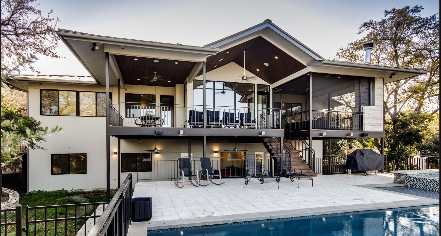 A modern two-story home with a multi-level deck and covered patio overlooking a backyard swimming pool and trees.