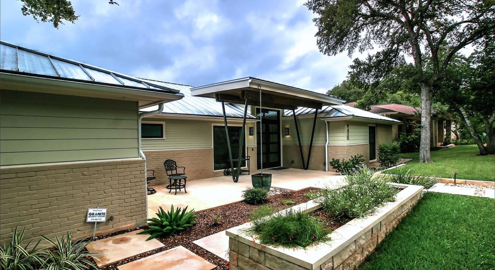 Modern house with patio, green and beige exterior, metal roof, and landscaped yard.
