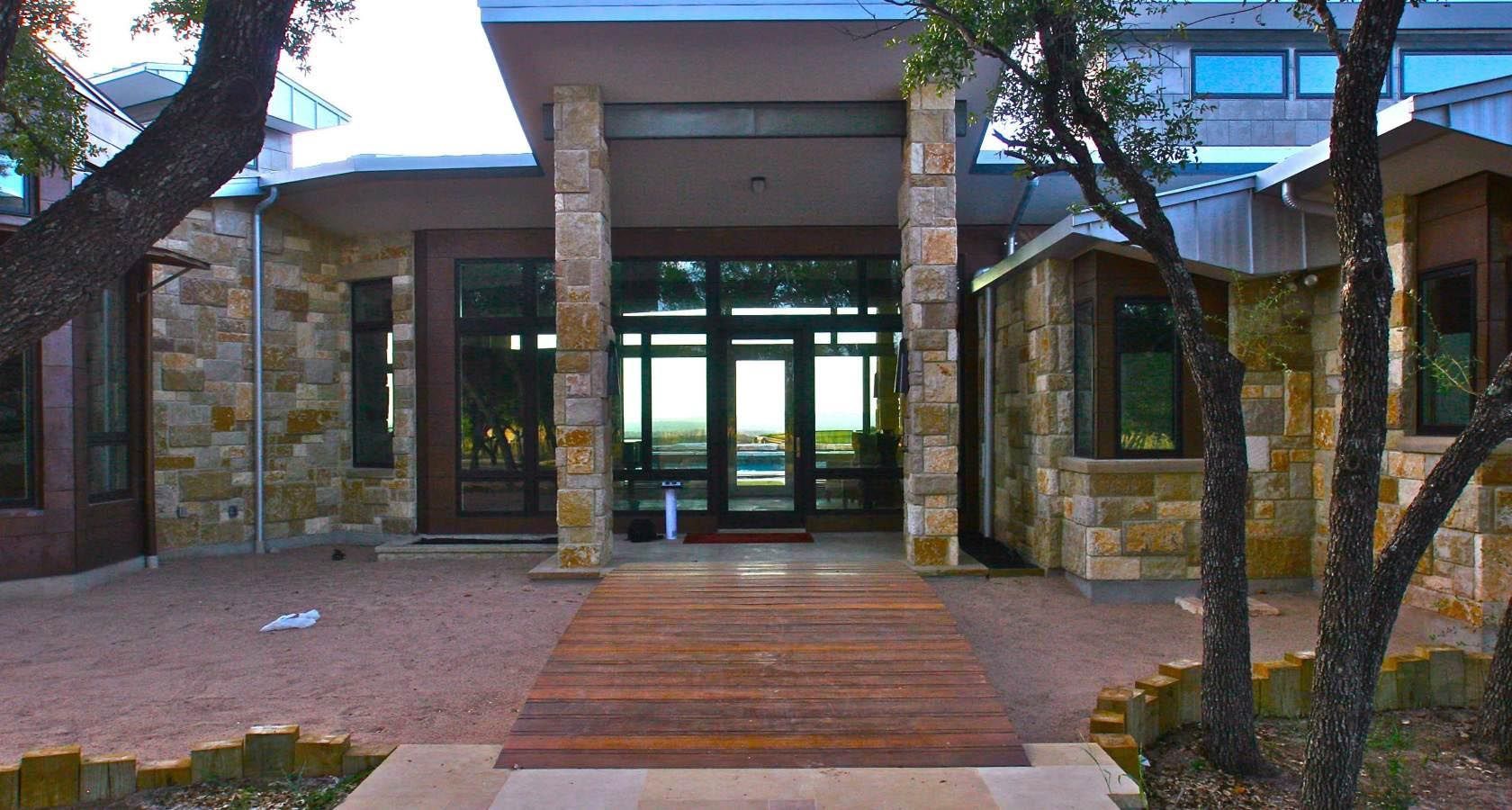 Stone and glass house entrance with wooden pathway.