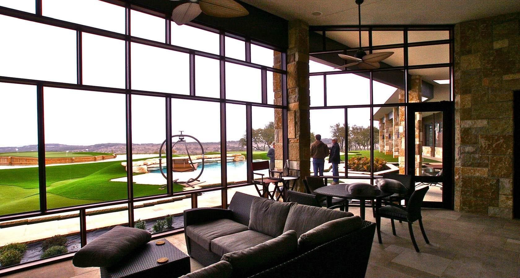 Patio with a view: Glass walls frame a pool and golf course. A sofa and table are inside.