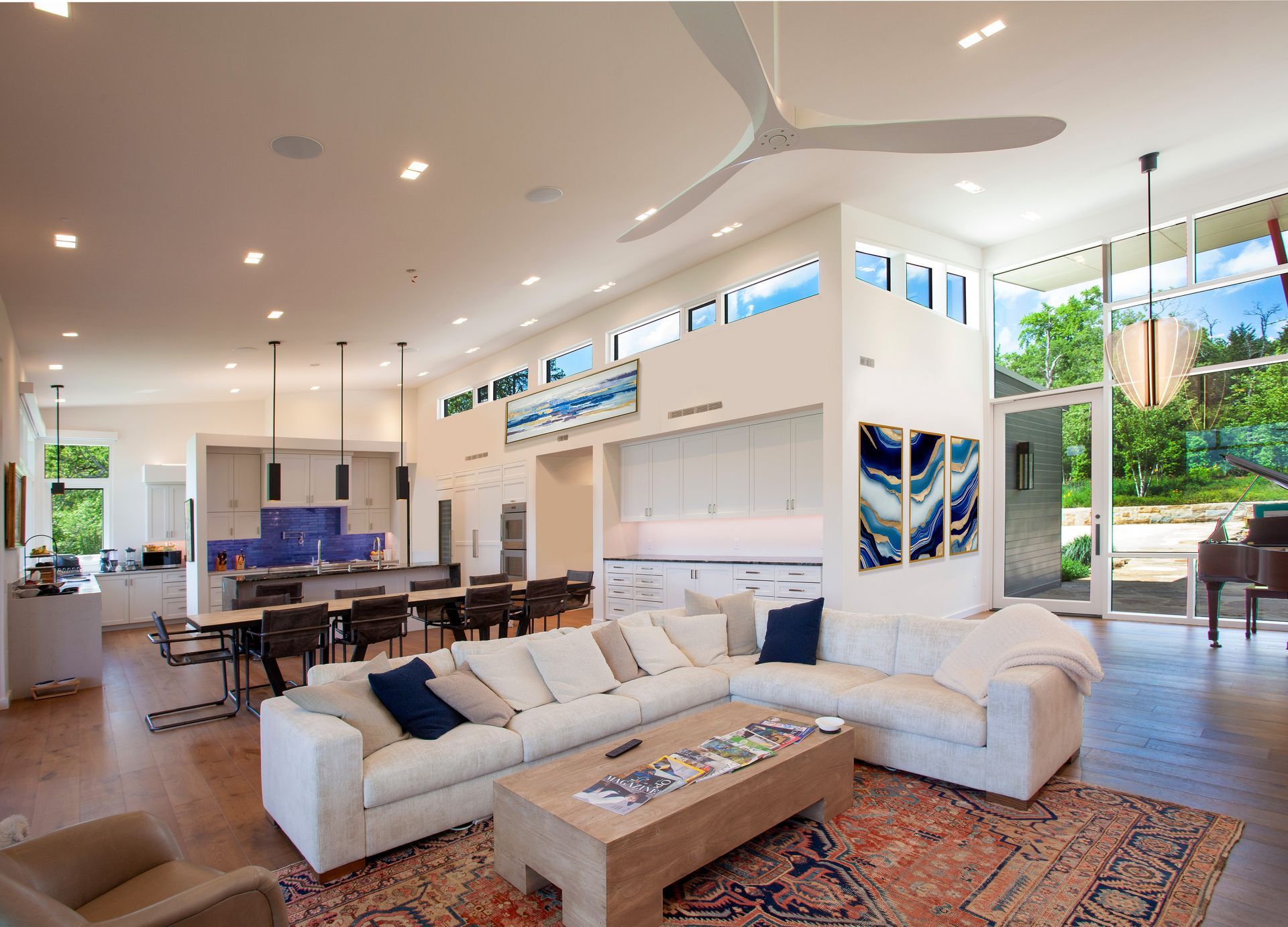 A spacious, modern open-plan living and dining area with a large white sectional, wooden coffee table, and blue accents.