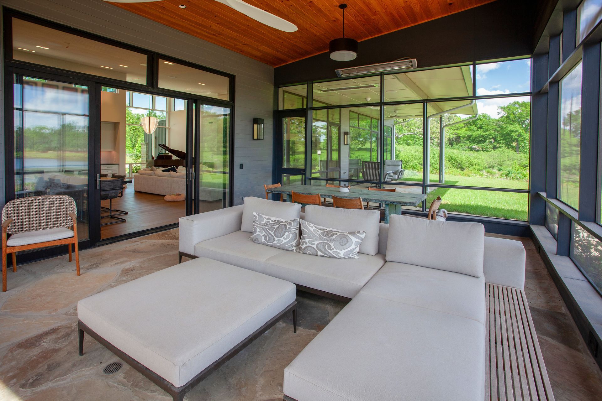 A modern, screened-in porch with light-colored sectional seating, a matching ottoman, and a view of a lush green backyard.