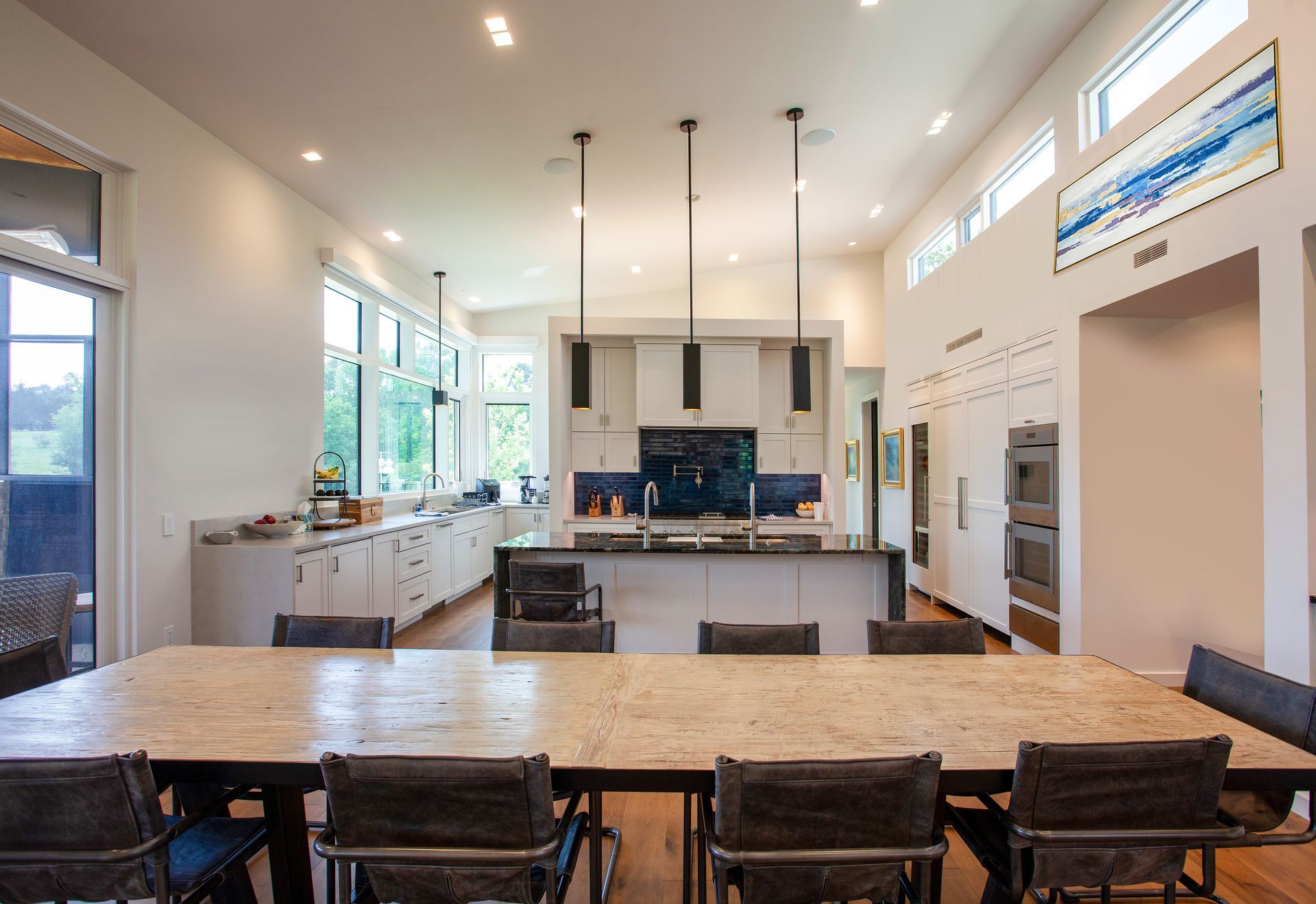 A modern, bright open-plan kitchen with a long wooden dining table and chairs in the foreground.