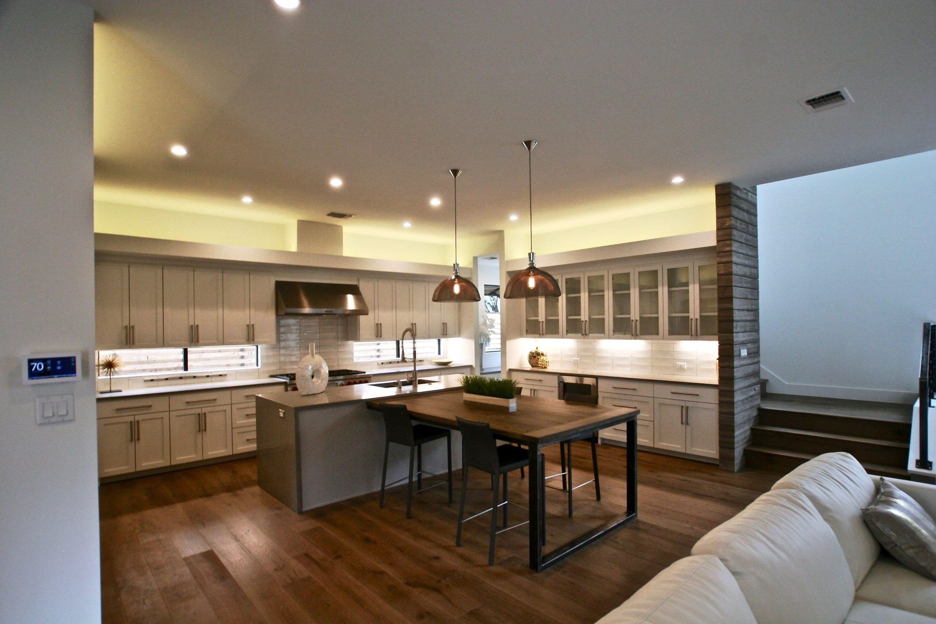 Modern kitchen with light gray cabinets, island with stools, hardwood floors, and pendant lights.