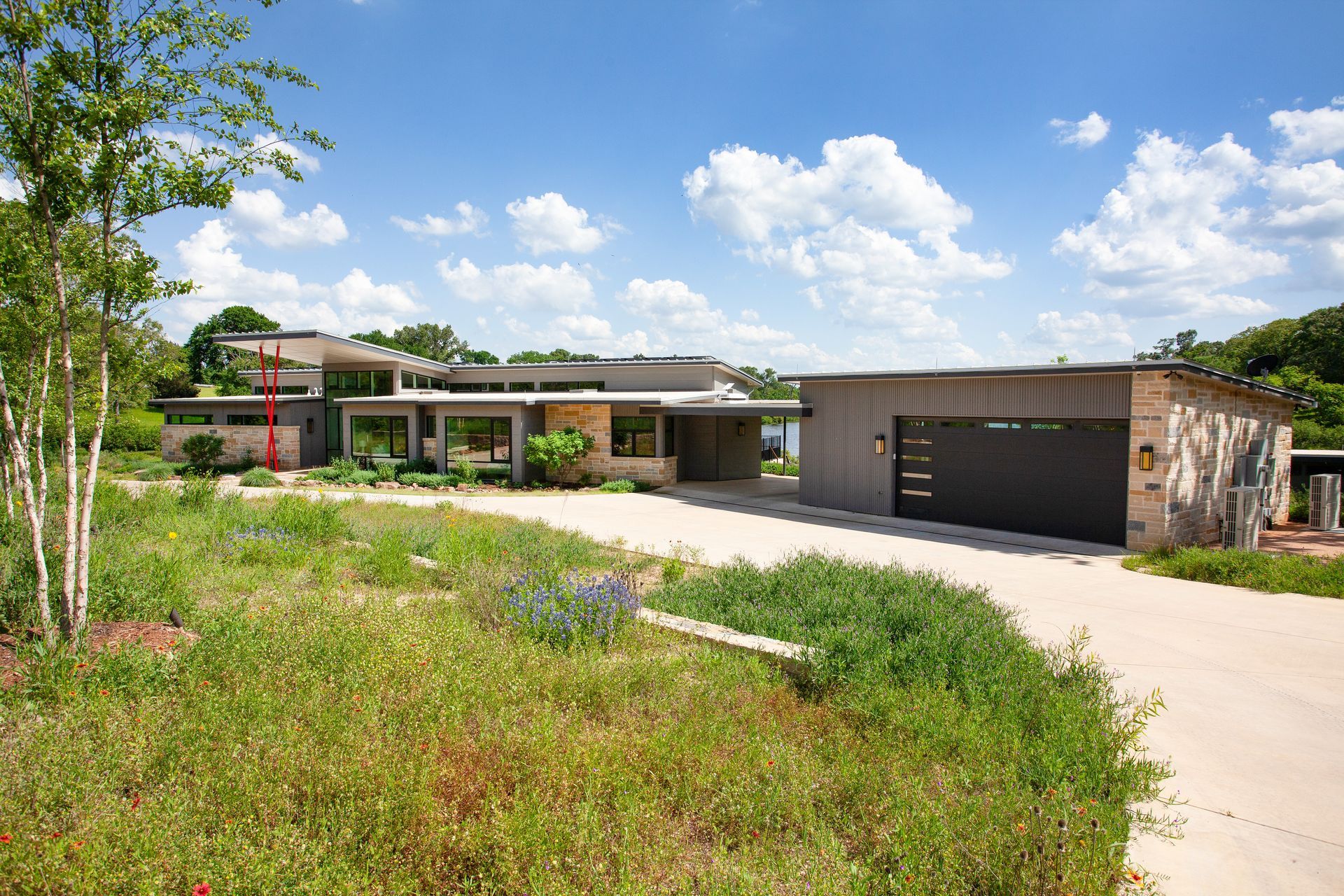 A modern, low-slung house with a flat roof, large windows, and an attached garage set in a grassy, landscaped yard.