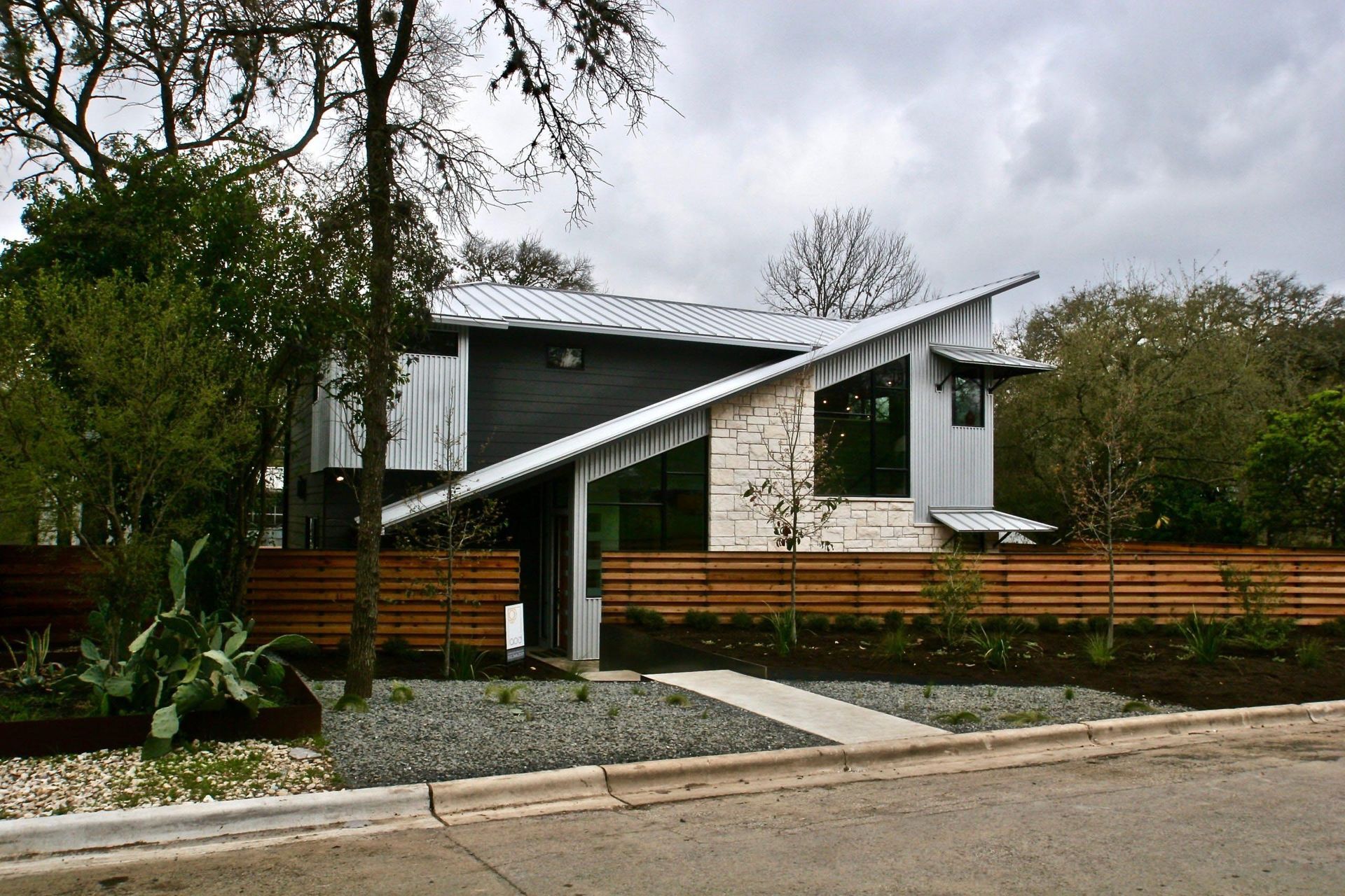 Modern house with angled roof, horizontal wood fence, stone facade, and landscaping.