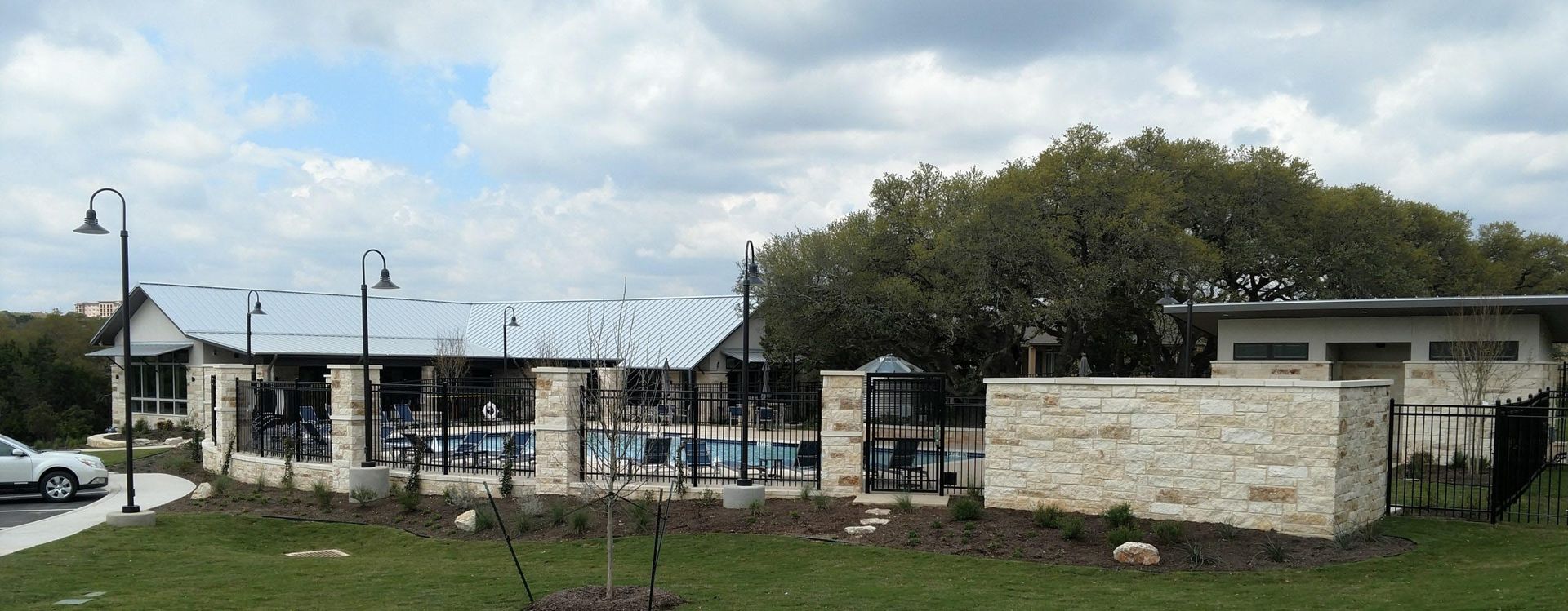 A building with a pool, stone walls, and a large tree under a cloudy sky.