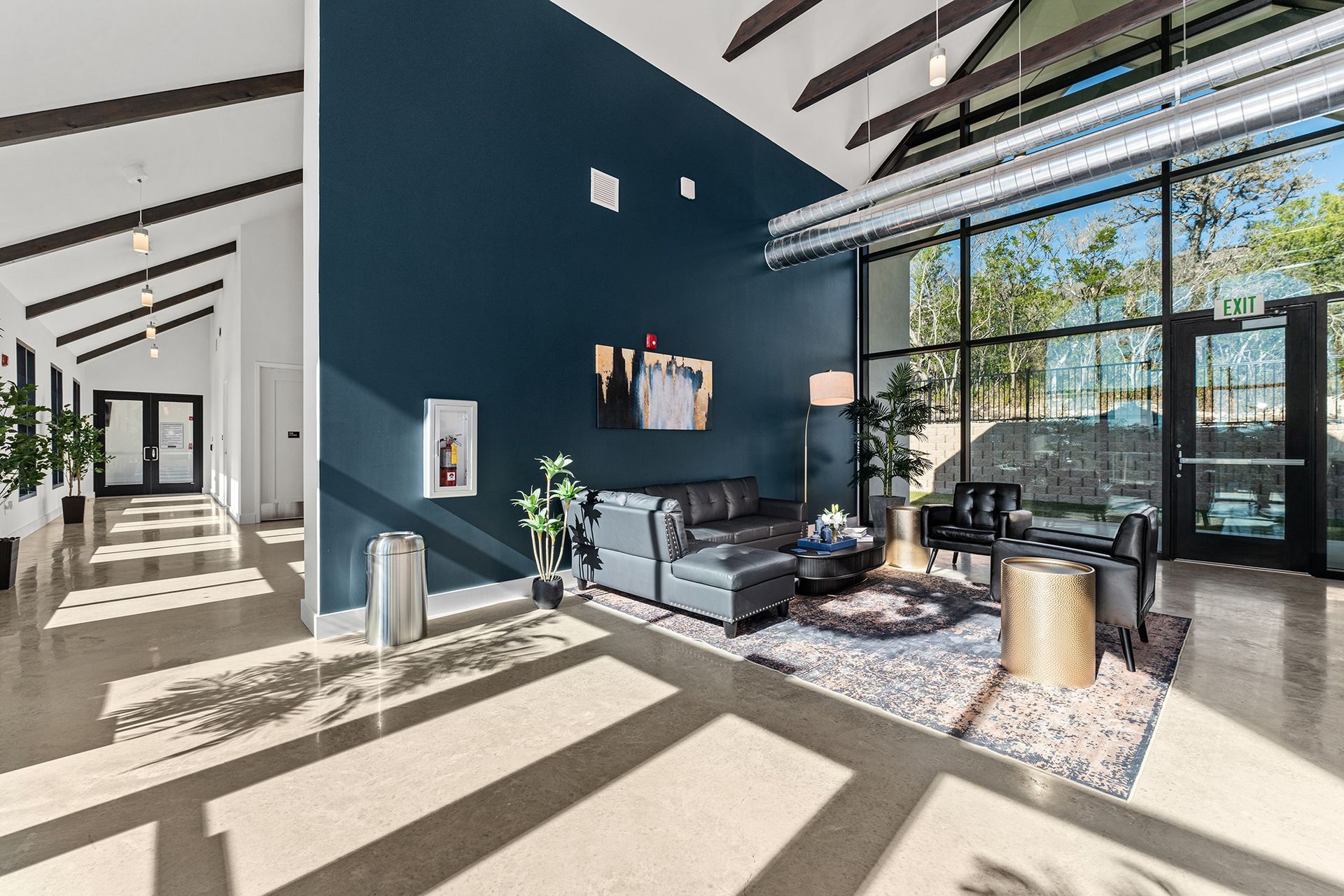 A modern lounge with dark blue walls, a gray sectional, two chairs, a round coffee table, and large windows.