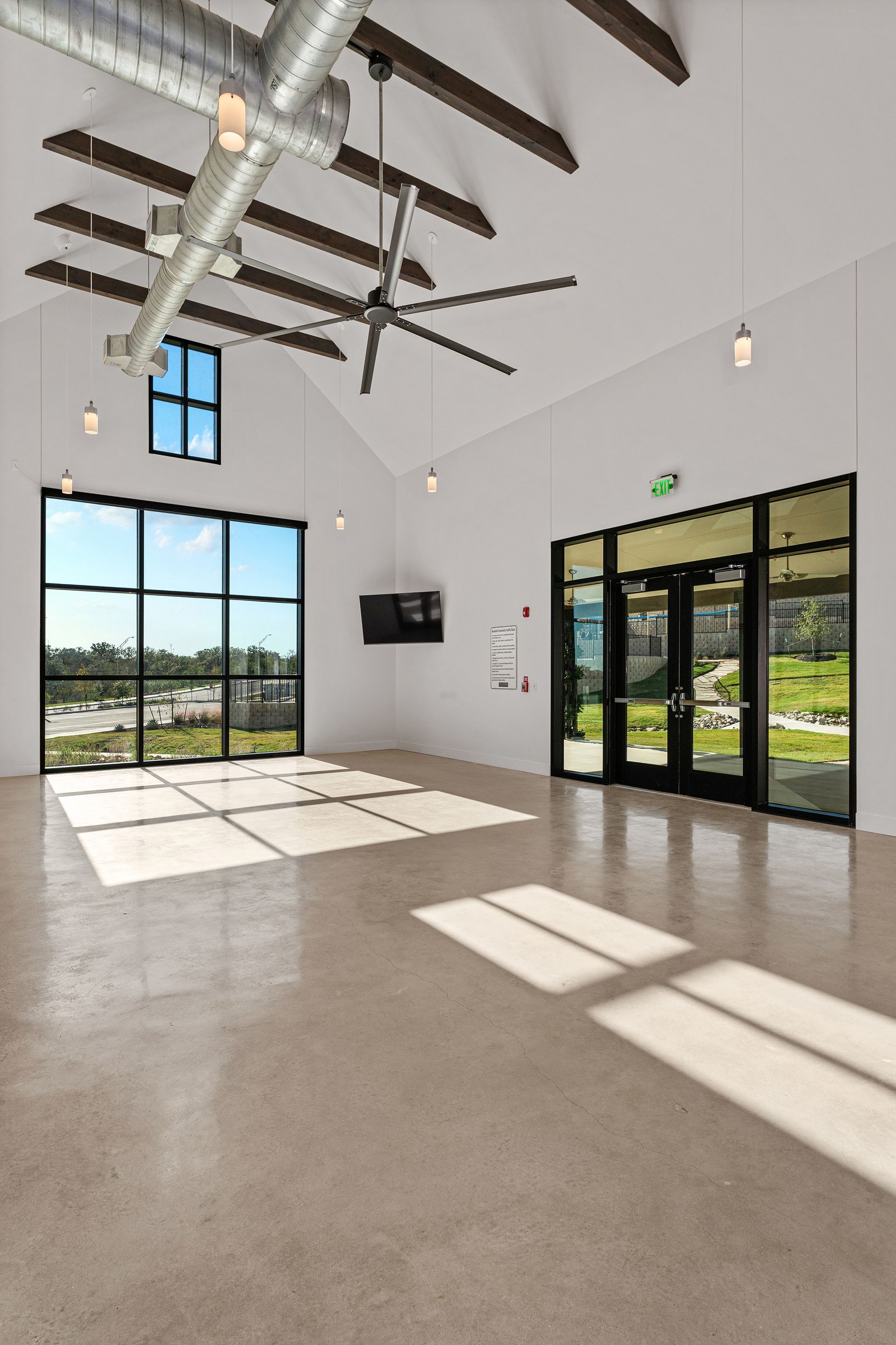 An empty, modern interior room with white walls, a high vaulted ceiling with exposed beams, polished floors, and windows.