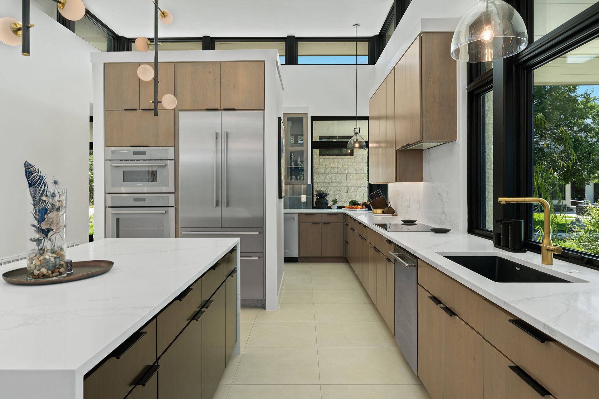 Modern kitchen with a white island, light wood cabinets, stainless steel appliances, and large windows.