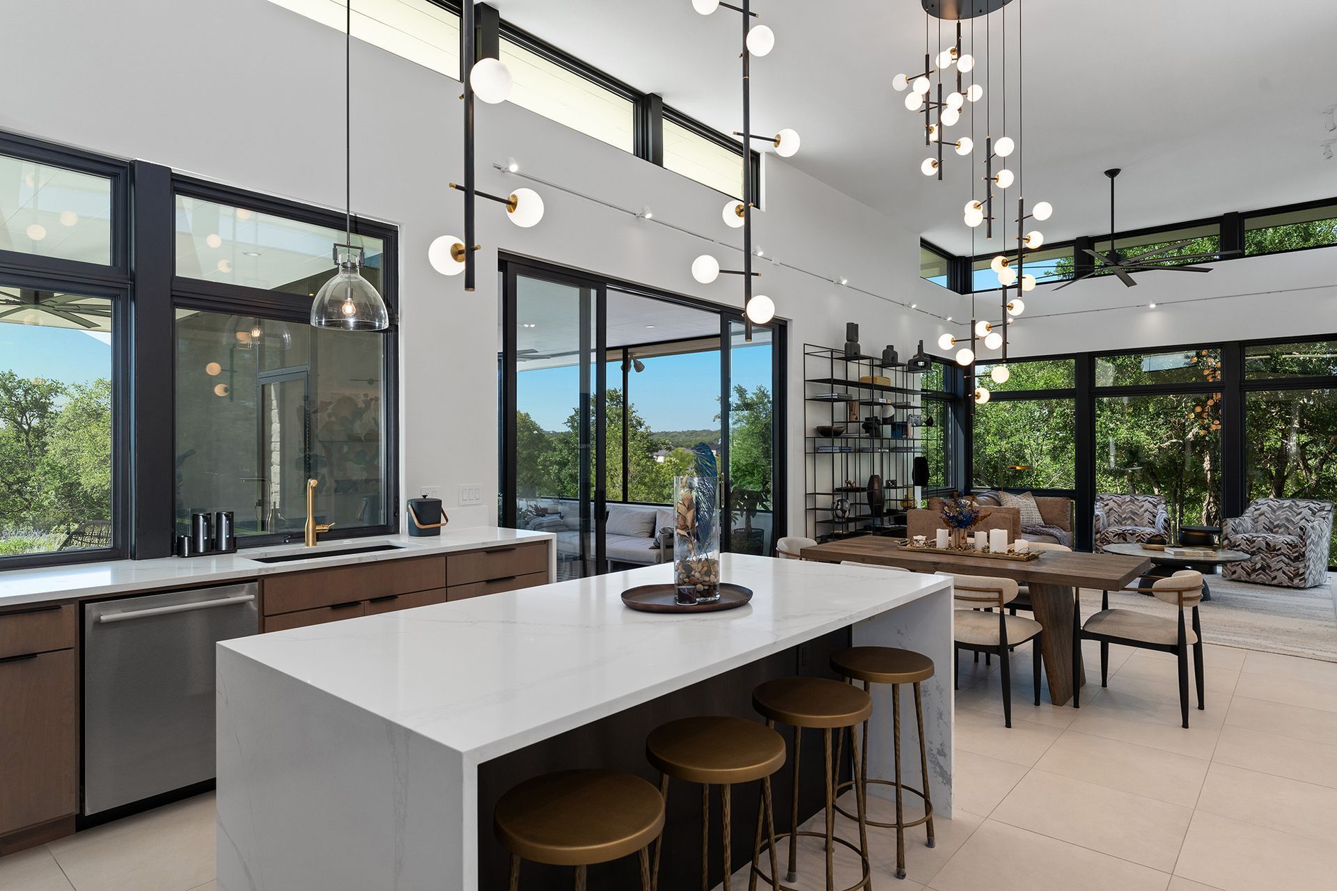 A modern open-plan kitchen and dining area with a white marble island, brown cabinets, and geometric light fixtures.