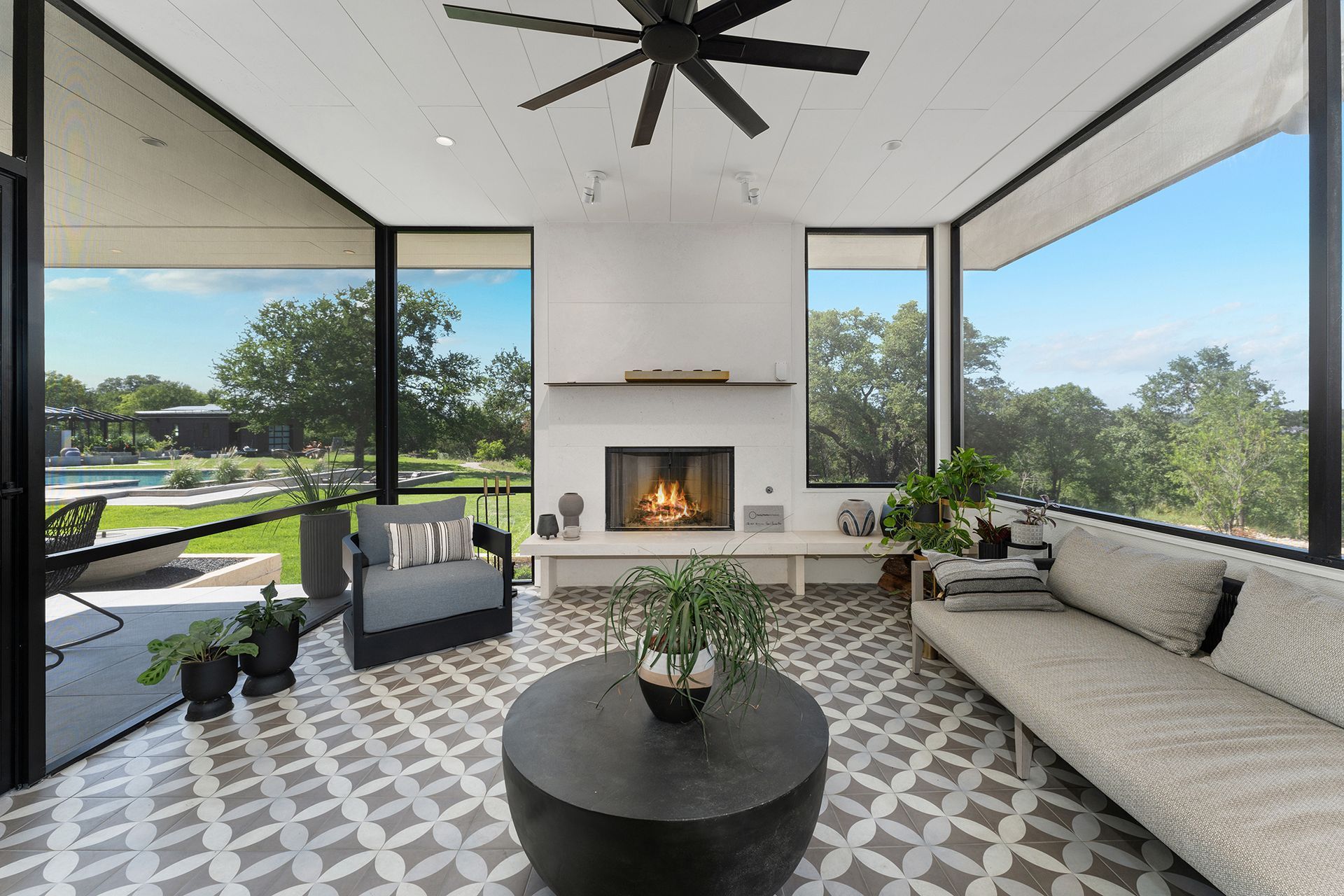 A bright, modern screened-in porch with a fireplace, patterned tile floors, a round coffee table, and comfortable seating.