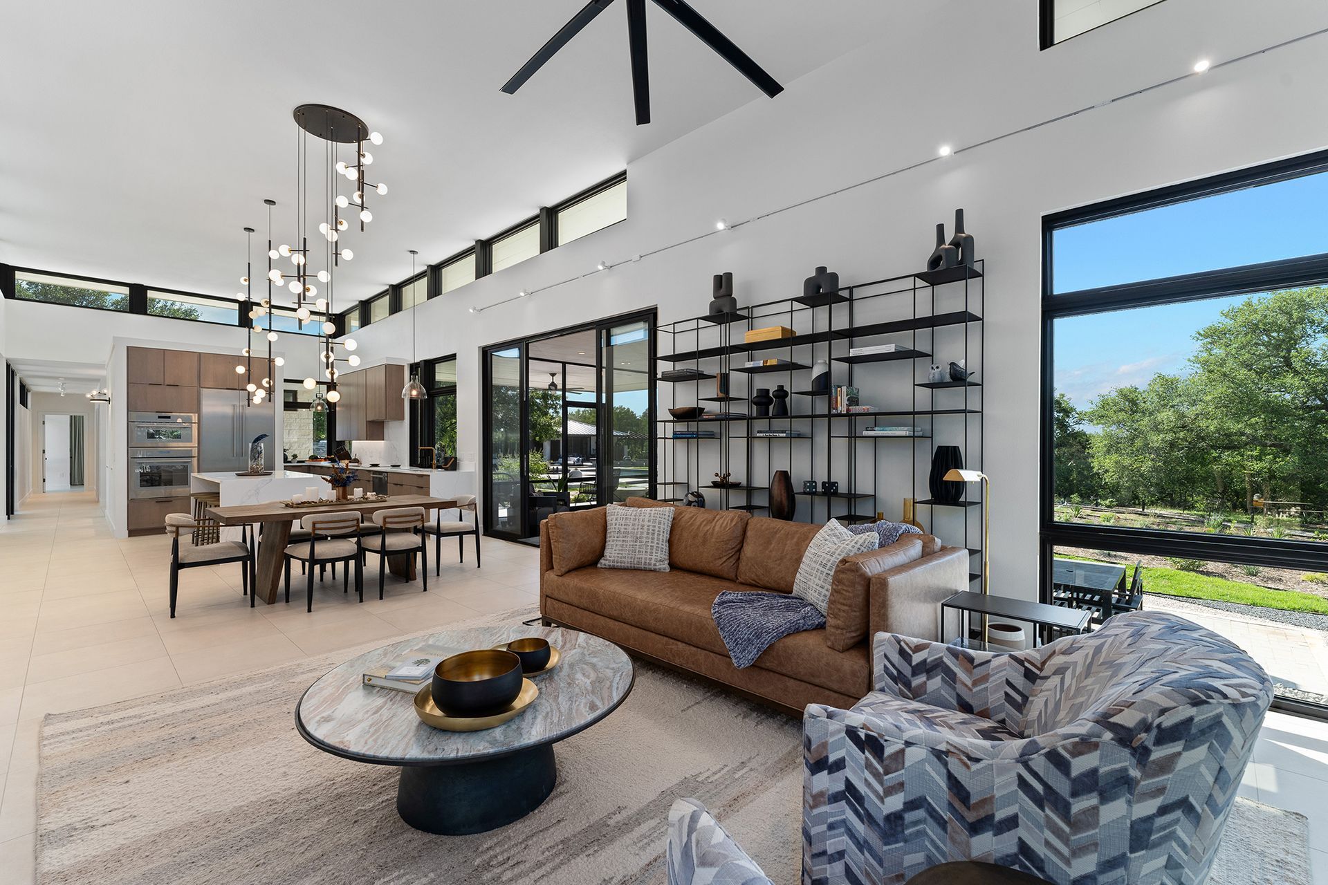 A bright, open-plan living room with a brown sofa, a patterned armchair, a round stone coffee table, and a dining area.