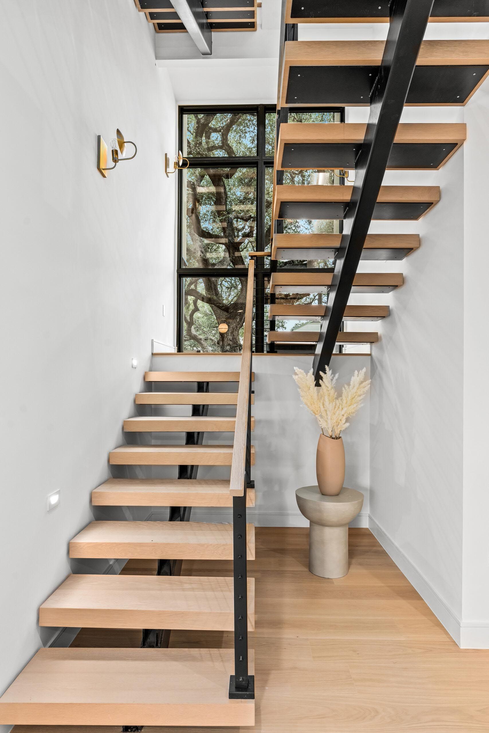 Staircase with wooden steps and black metal railing, next to a window with greenery.