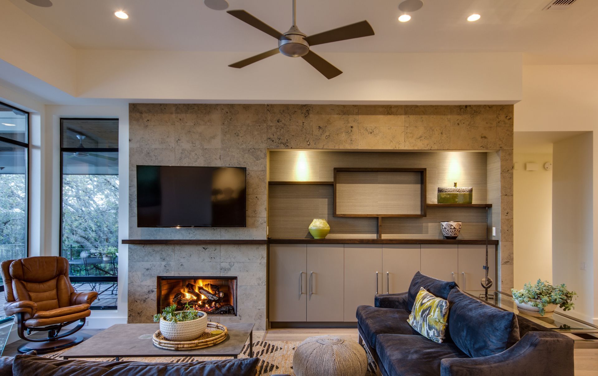 A cozy living room with a fireplace, TV, and stone wall feature, next to a navy sofa and a leather recliner.