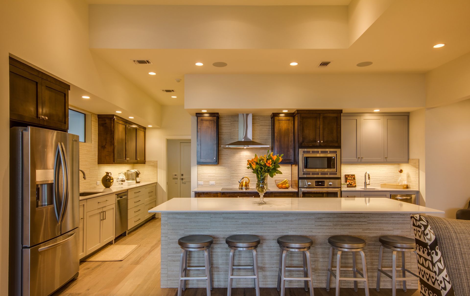 A modern kitchen with wood cabinets, light-colored countertops, a center island with five bar stools, and stainless steel.