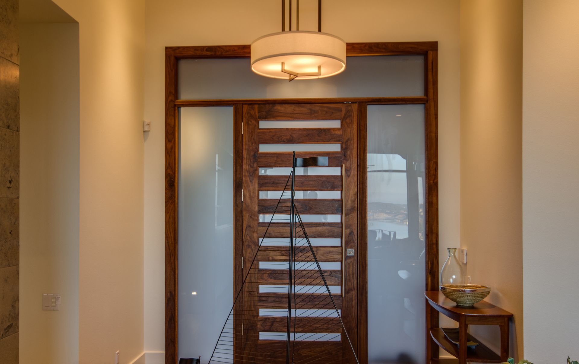 A wooden front door with horizontal glass panels, flanked by frosted glass sidelights, in a brightly lit home entryway.