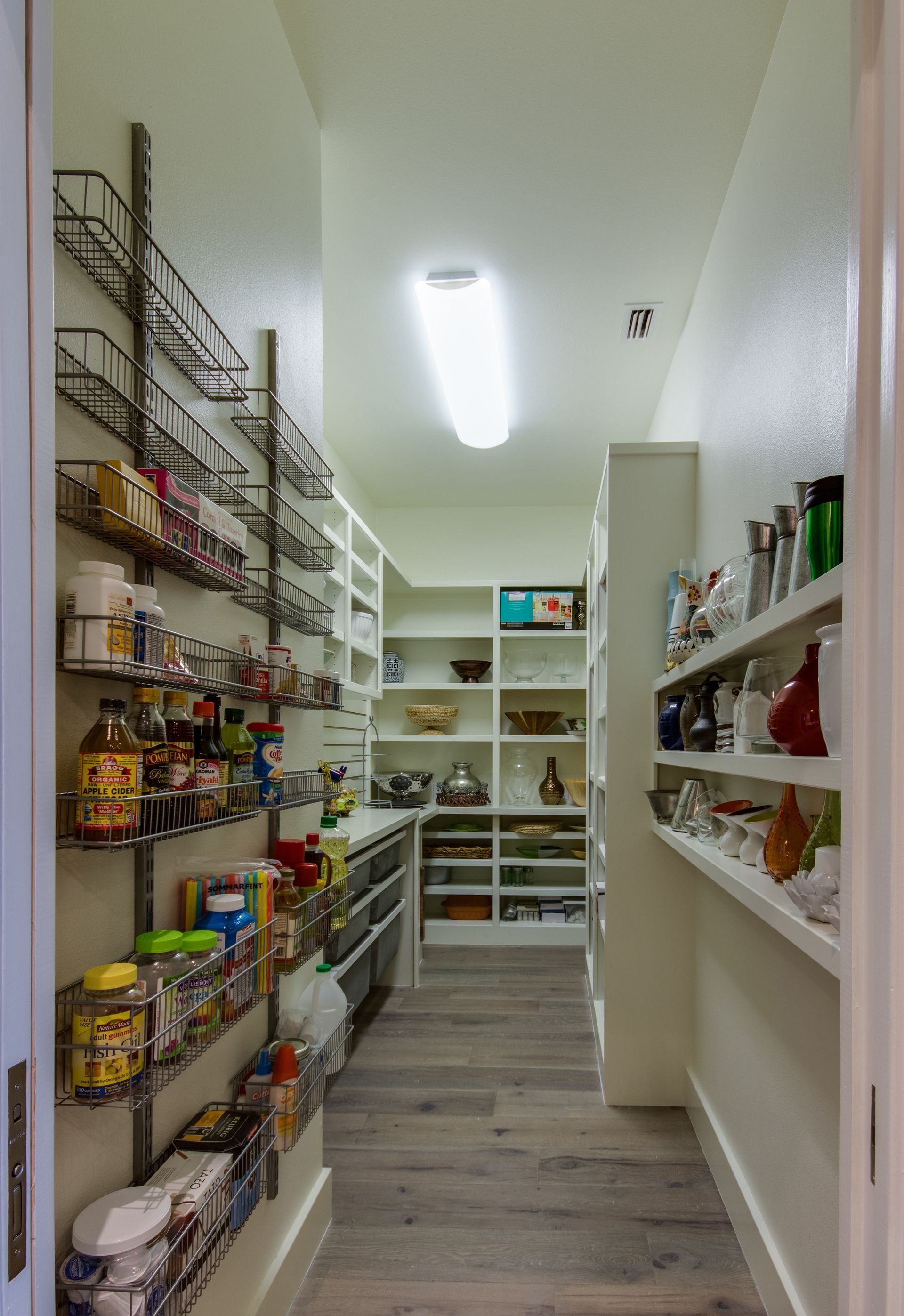 A walk-in pantry featuring metal wire wall racks on the left and white built-in shelves on the right and back.