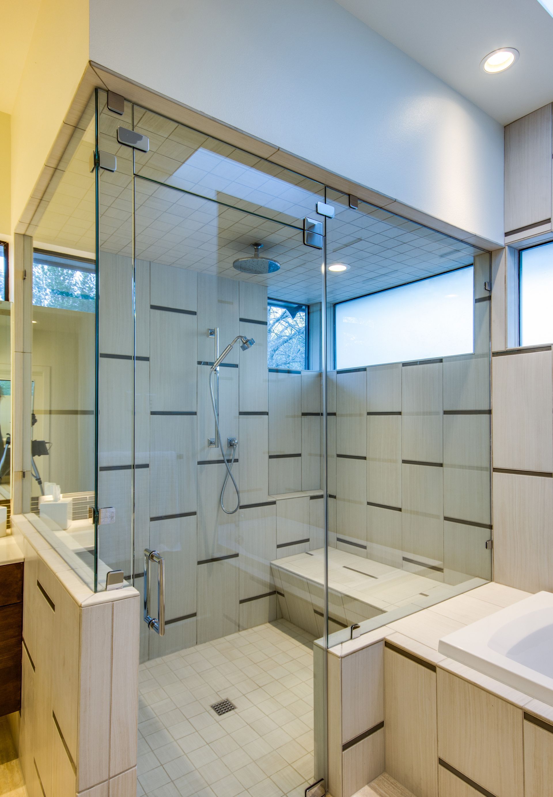 A modern glass-enclosed shower with light, horizontal-patterned tiles and a built-in bench seat.