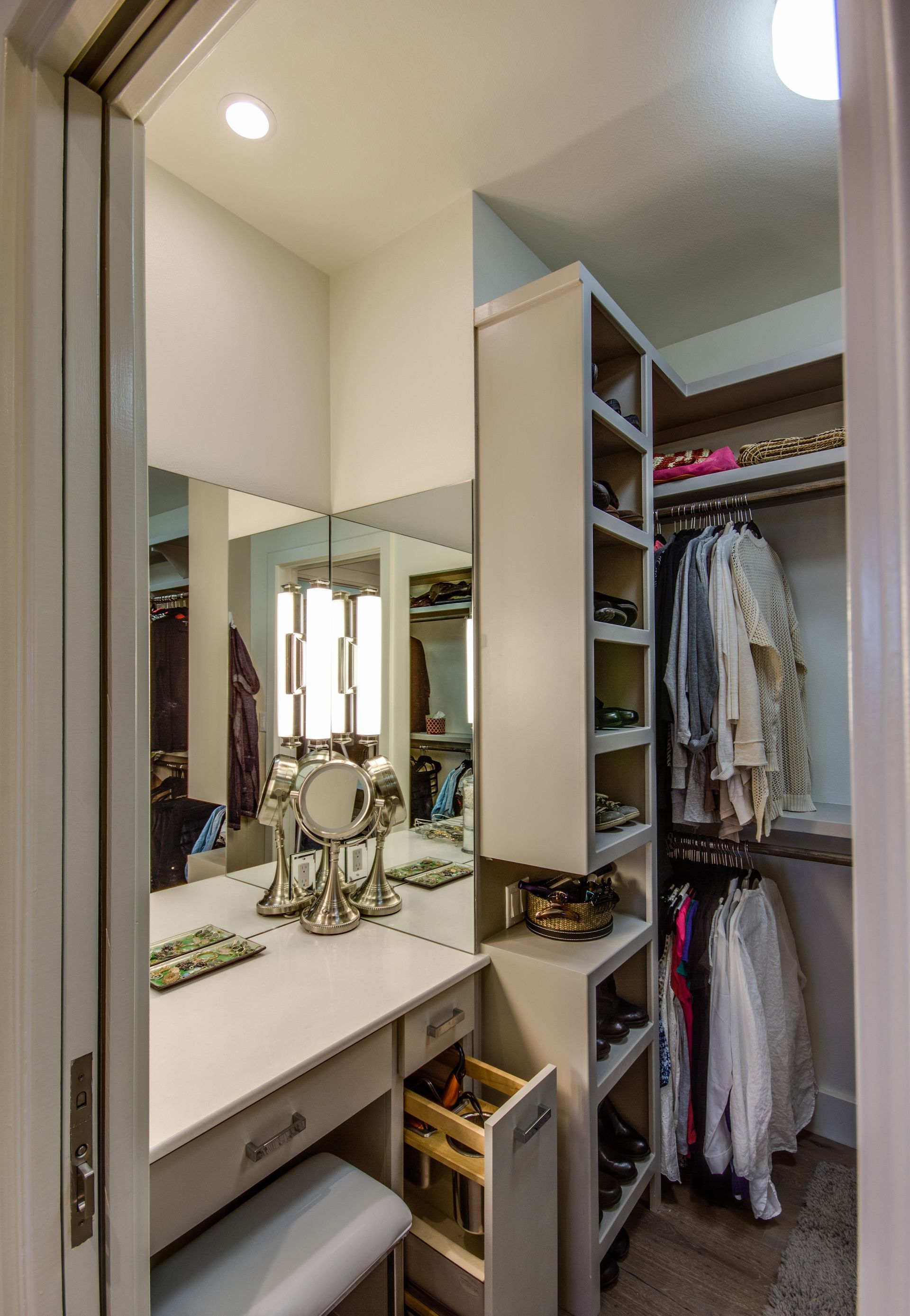 A walk-in closet featuring a vanity with a mirror, a built-in shelf unit for shoes, and a hanging clothing rack.