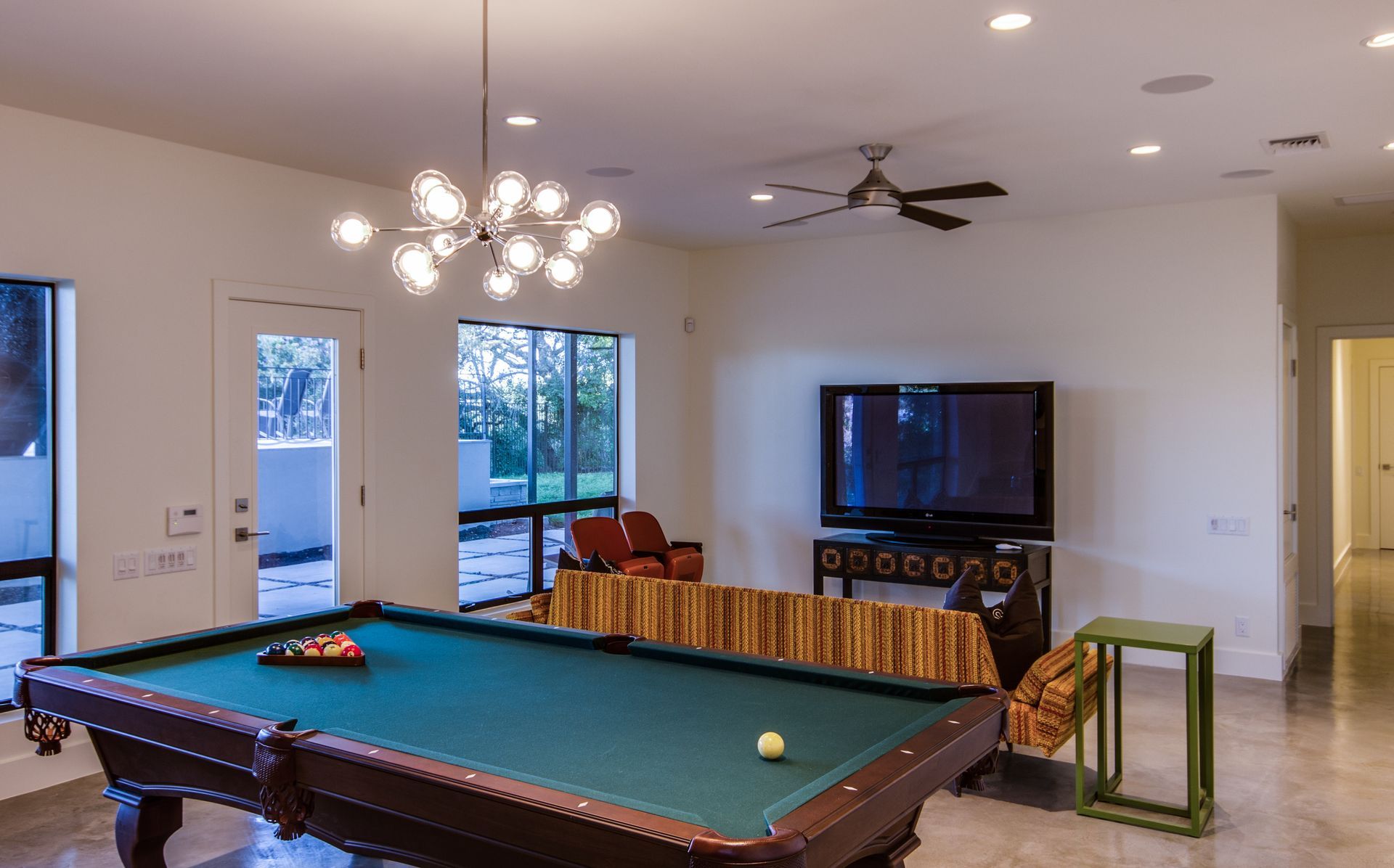 A billiards table in a spacious, modern room with a TV, a patterned sofa, and a contemporary chandelier.