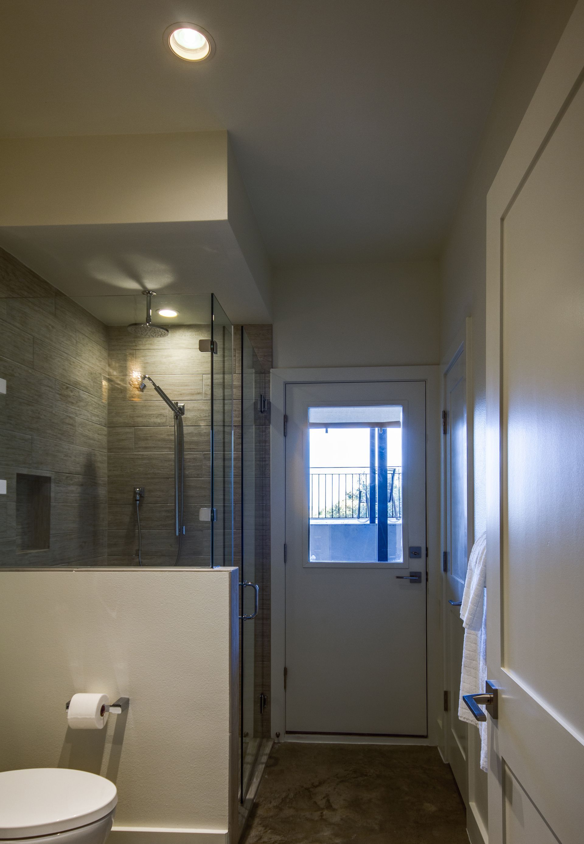 A bathroom features a glass-enclosed shower next to a white toilet and a door with a window looking outside.