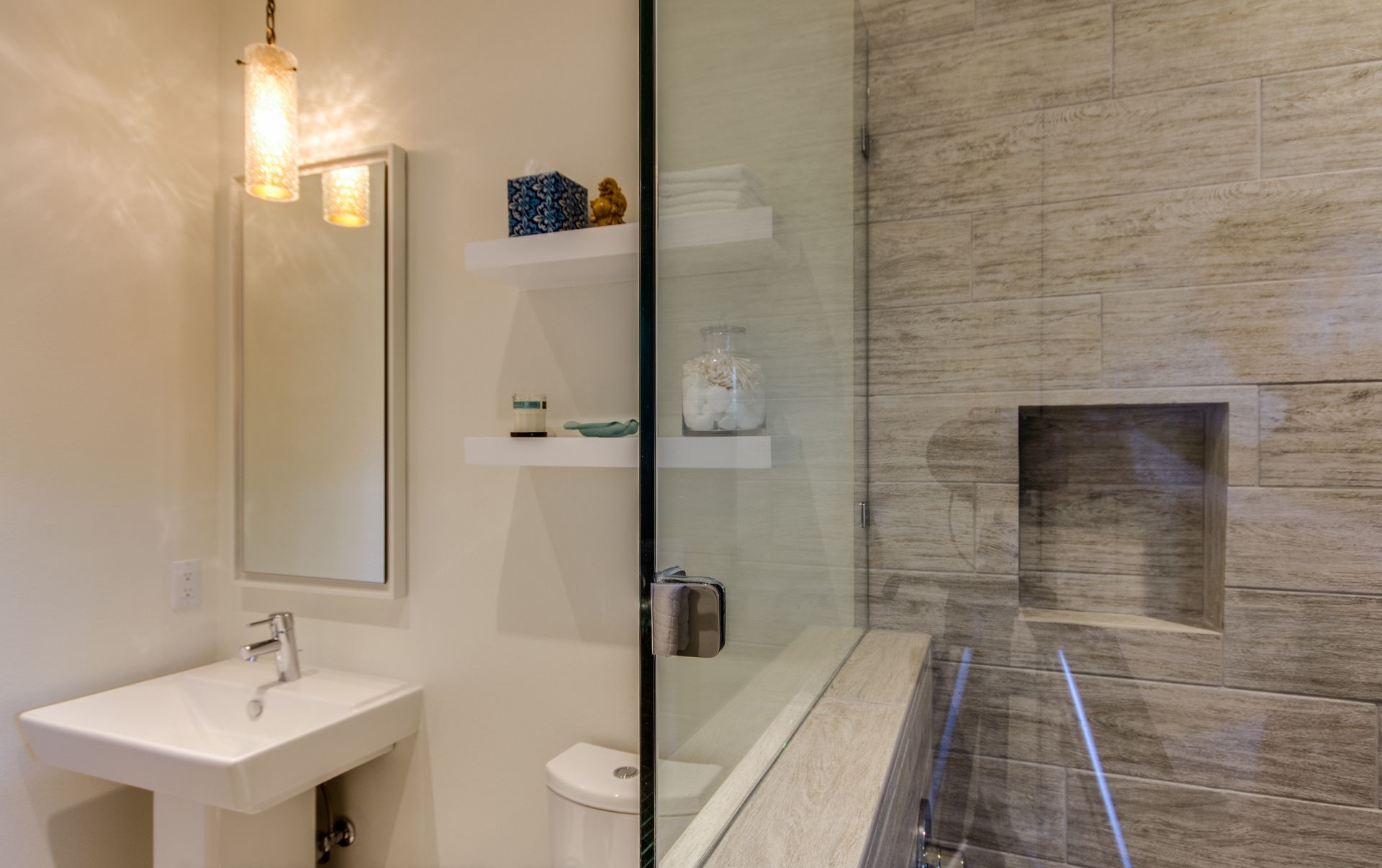 Modern bathroom featuring a pedestal sink, a glass-enclosed shower with stone tile, and built-in floating wall shelves.