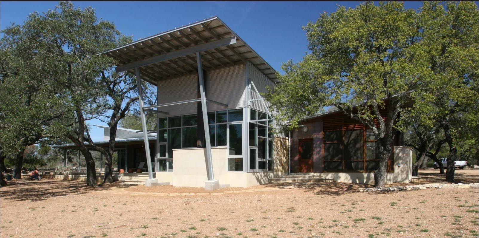 Modern building with large windows, angled roof, and trees in a dry, outdoor setting.