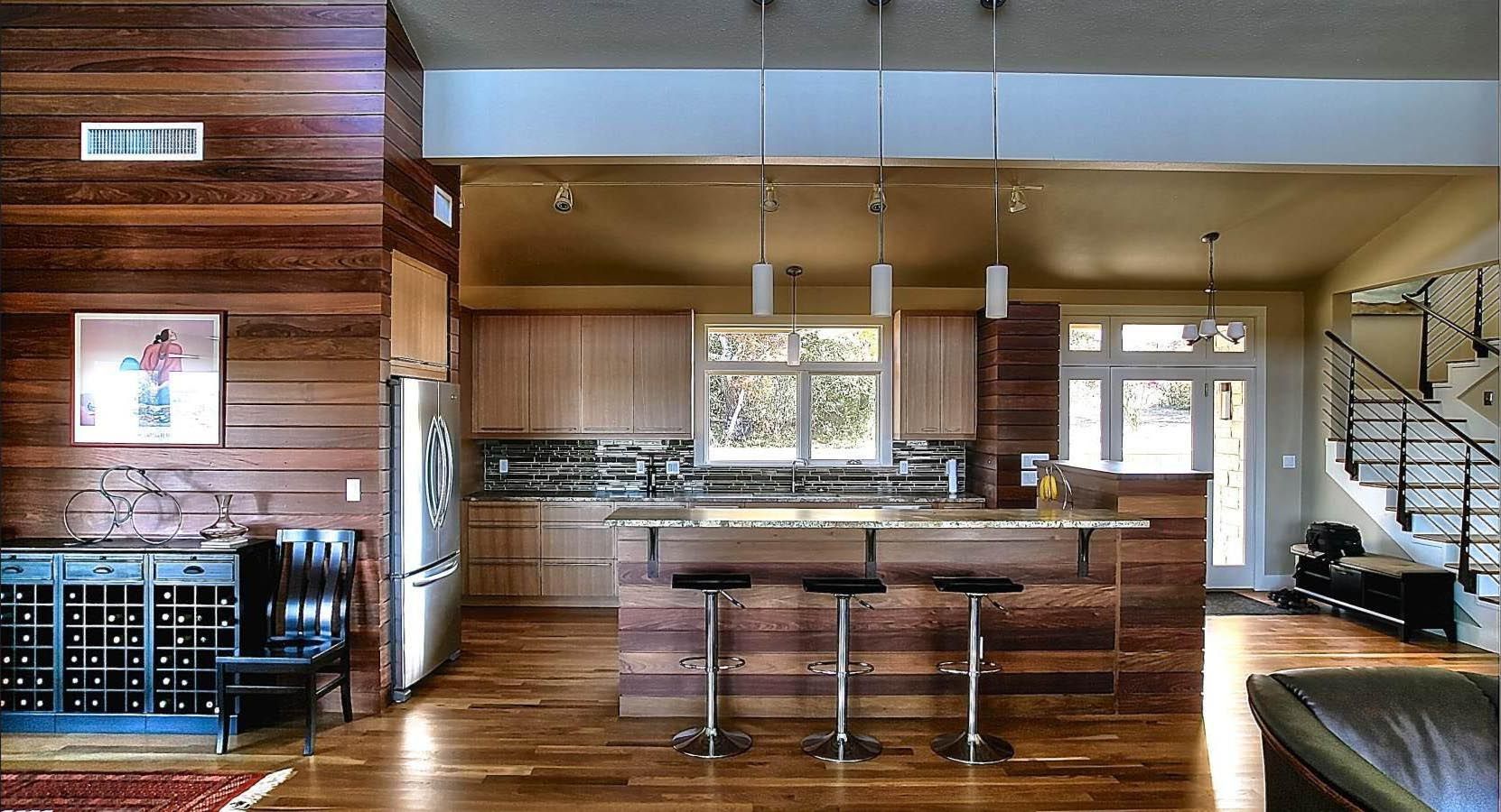 Modern kitchen with wood paneling, island with bar stools, and a staircase.