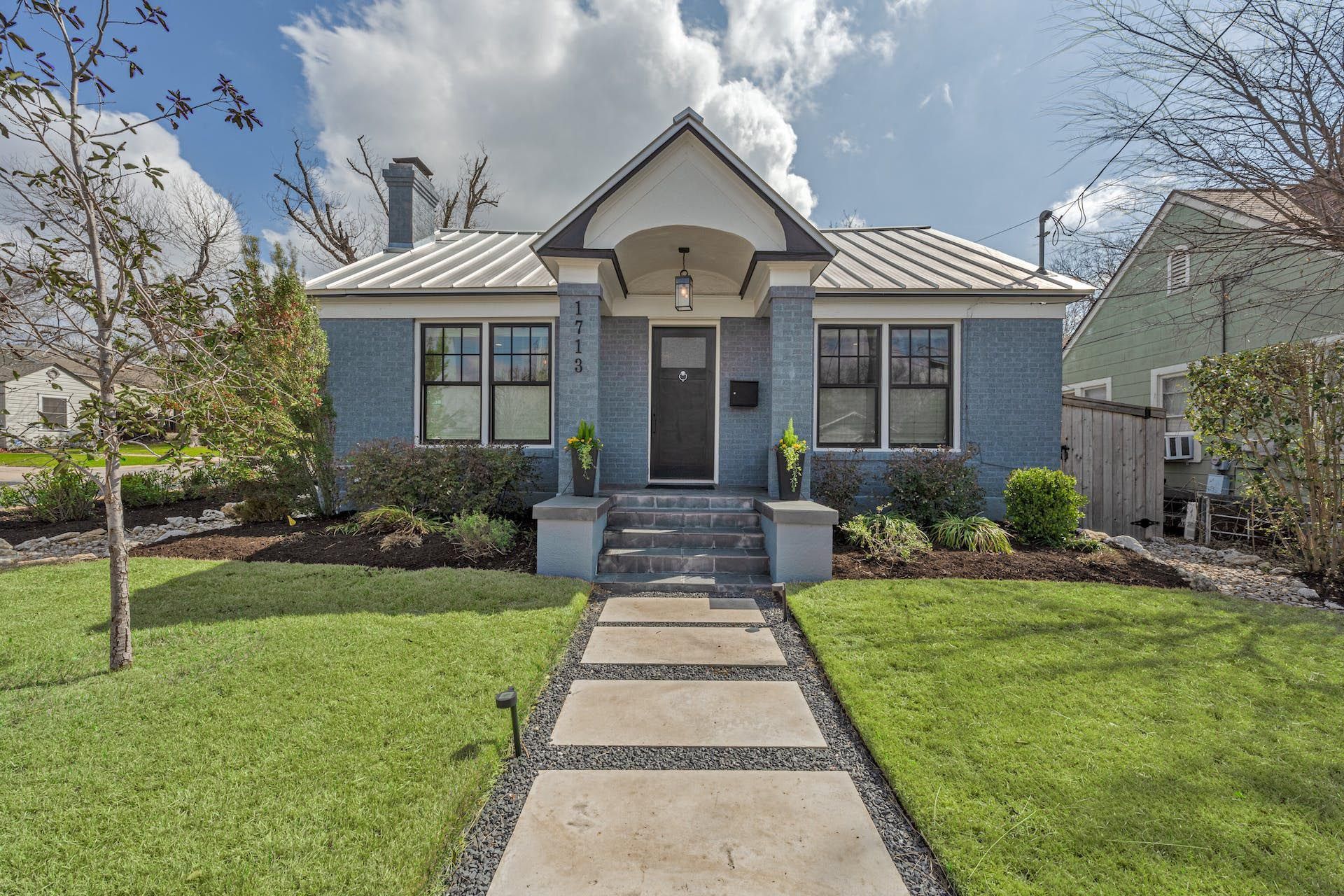 Blue house with white trim, gray steps, and a walkway through the green lawn.