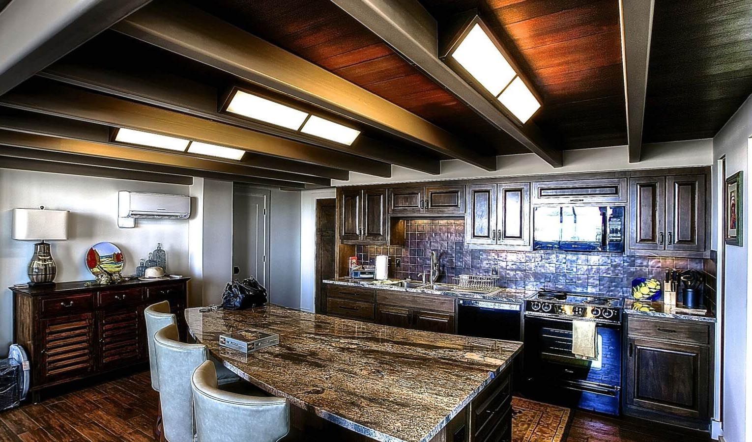 Kitchen with granite island, wooden cabinets, and exposed beams.