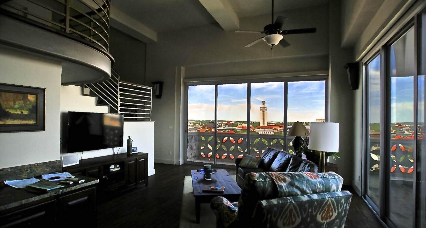 Loft interior with city view. Living room with dark furniture, large windows, and a spiral staircase