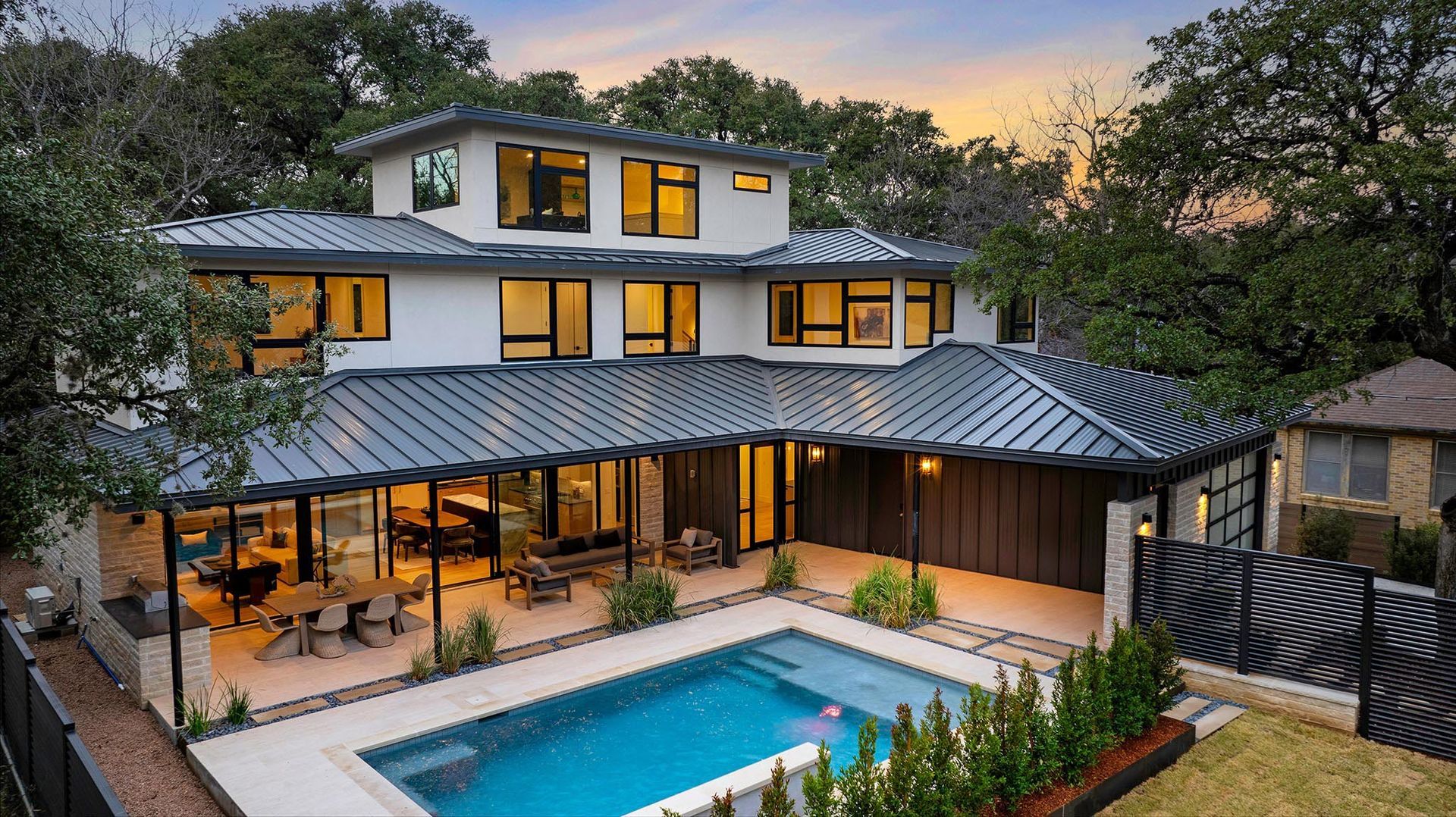 Modern multi-story house with a pool in a yard surrounded by trees.