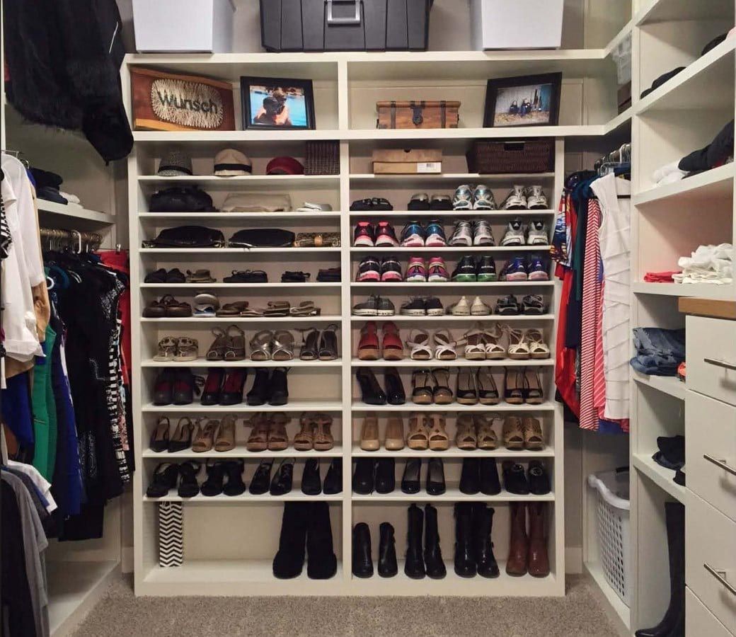 Closet with shoe shelves holding various pairs of footwear. White shelves and storage.