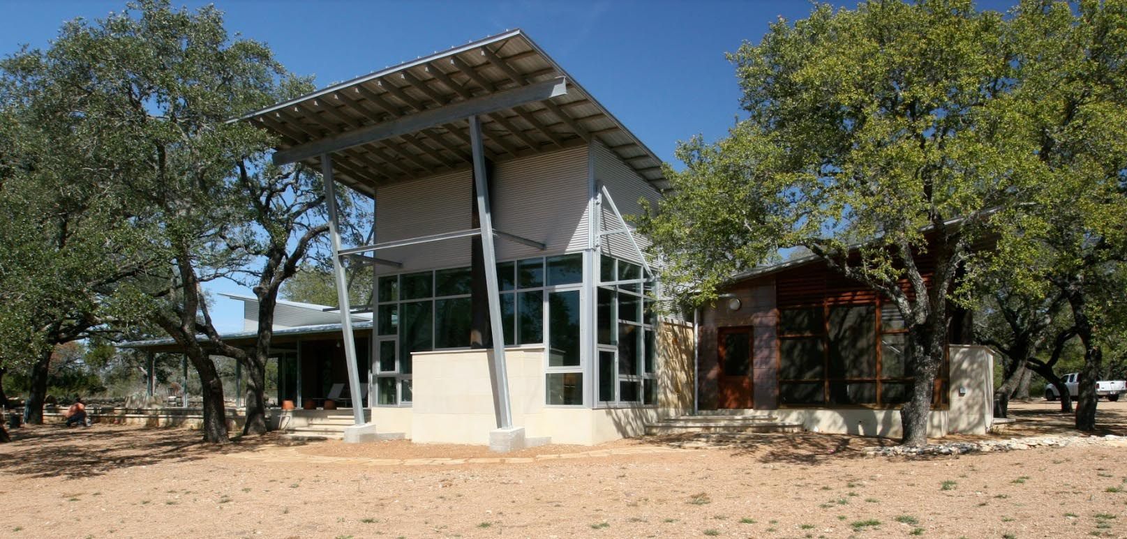 Modern building with slanted roof, glass windows, and metal supports surrounded by trees.