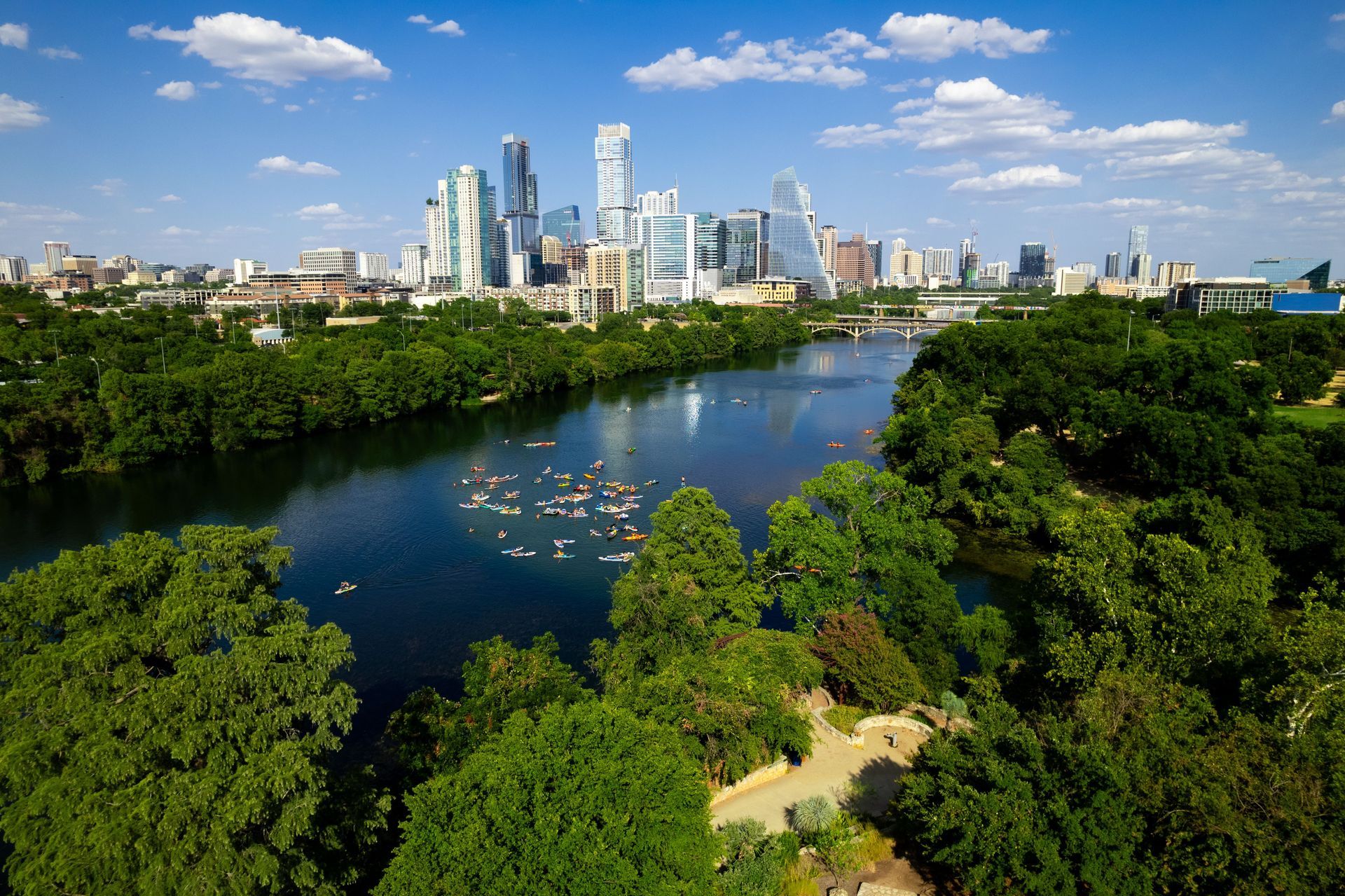 City skyline above a river and lush green park under a blue sky