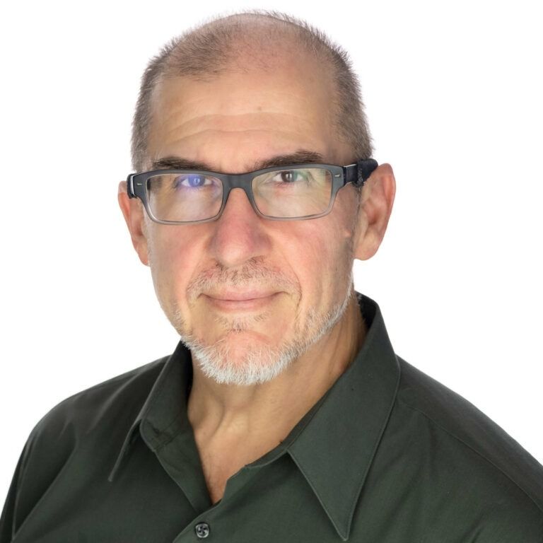A portrait of a bald person wearing glasses and a dark green collared shirt against a white background.