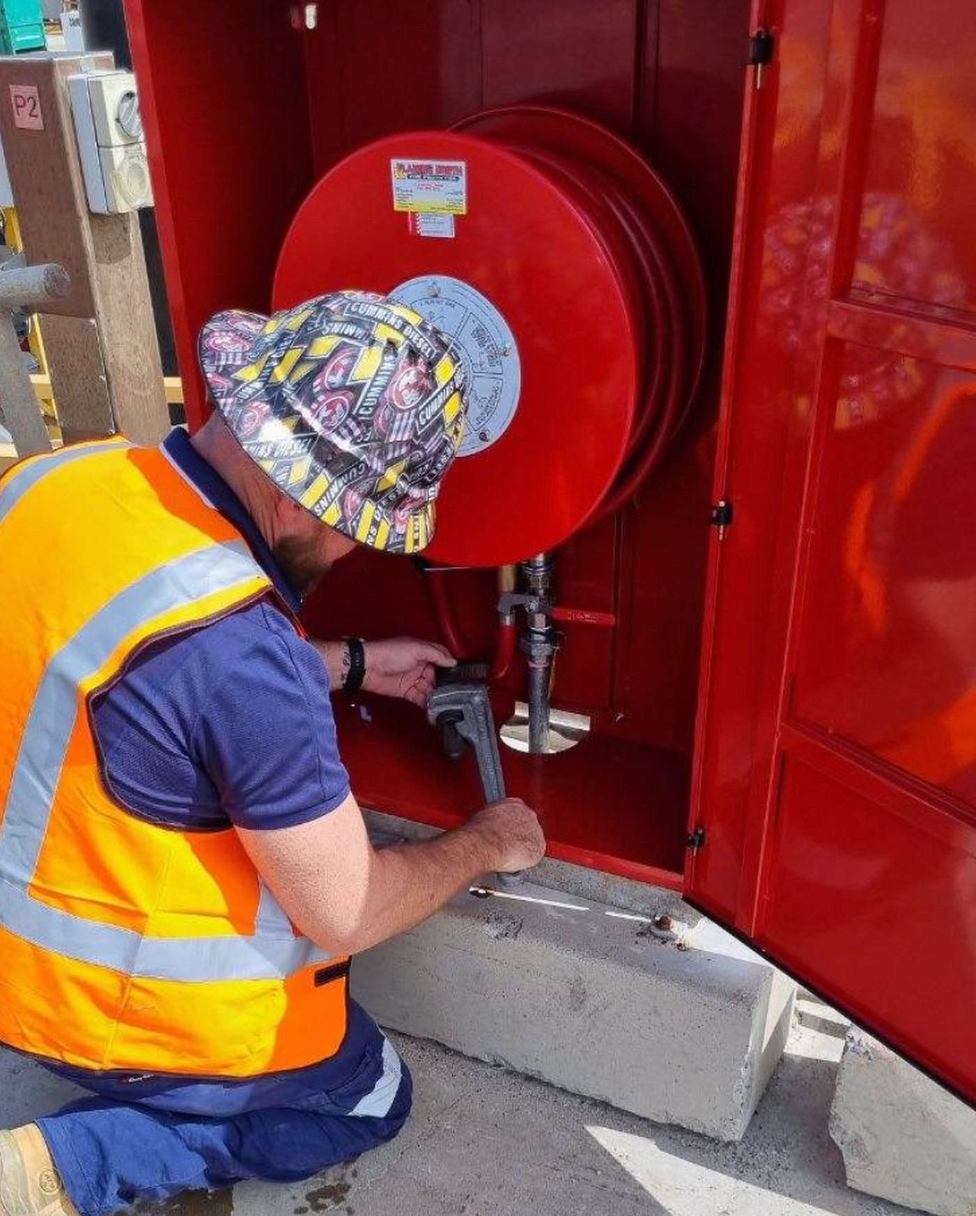 Worker In Reflective Vest and Hat Using a Hose at a Red Fire Safety Cabinet Outdoors — Flaming North Fire Protection Pty Ltd in Garbutt, QLD