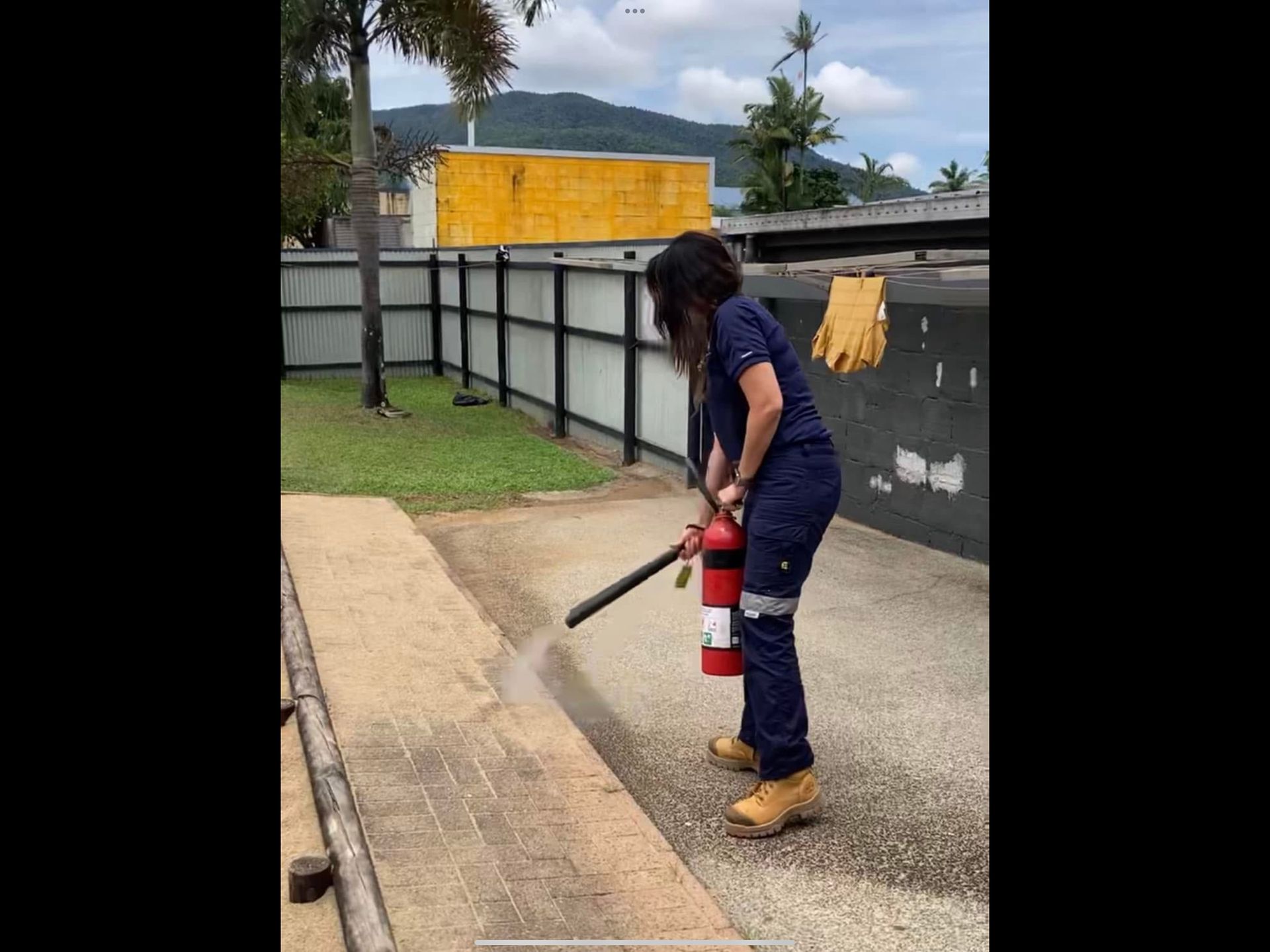 Person In Blue Uniform Using a Fire Extinguisher on a Paved Walkway Outdoors — Flaming North Fire Protection Pty Ltd in Innisfail, QLD