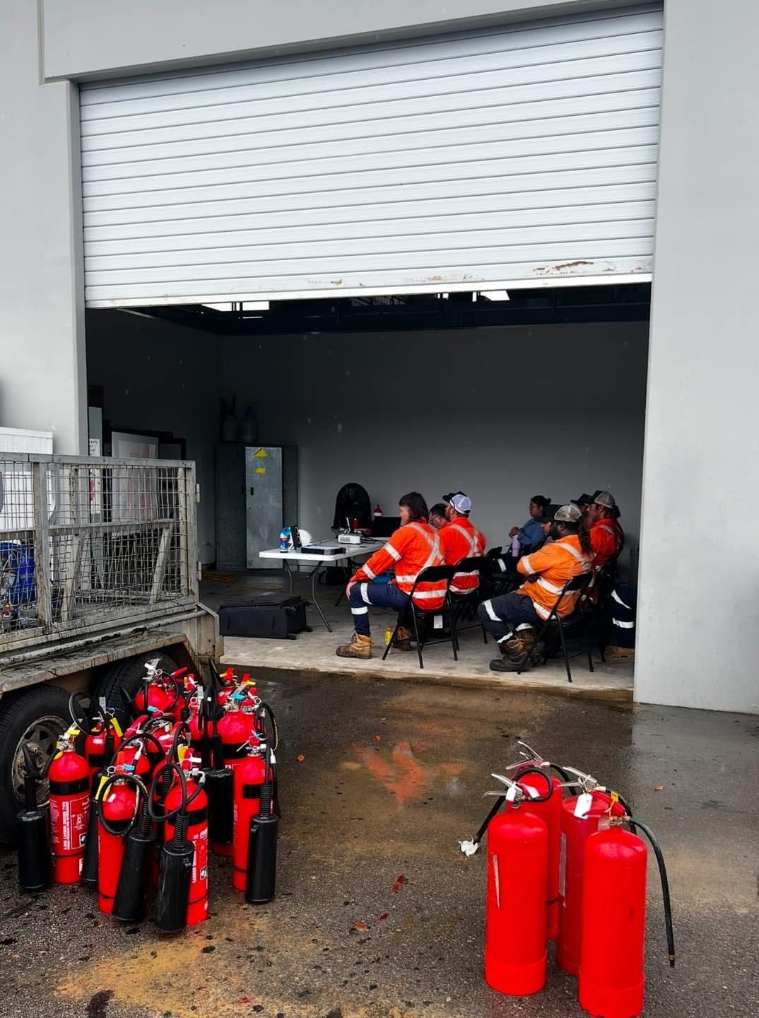 Person Using a Red Fire Extinguisher on a Sidewalk Near a Fence and Building — Flaming North Fire Protection Pty Ltd in Garbutt, QLD