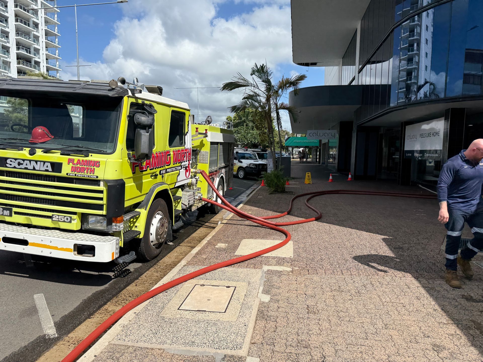 Yellow Fire Truck With Hoses Laid Out on a Street Beside a Building, With a Firefighter Nearby — Flaming North Fire Protection Pty Ltd in Garbutt, QLD