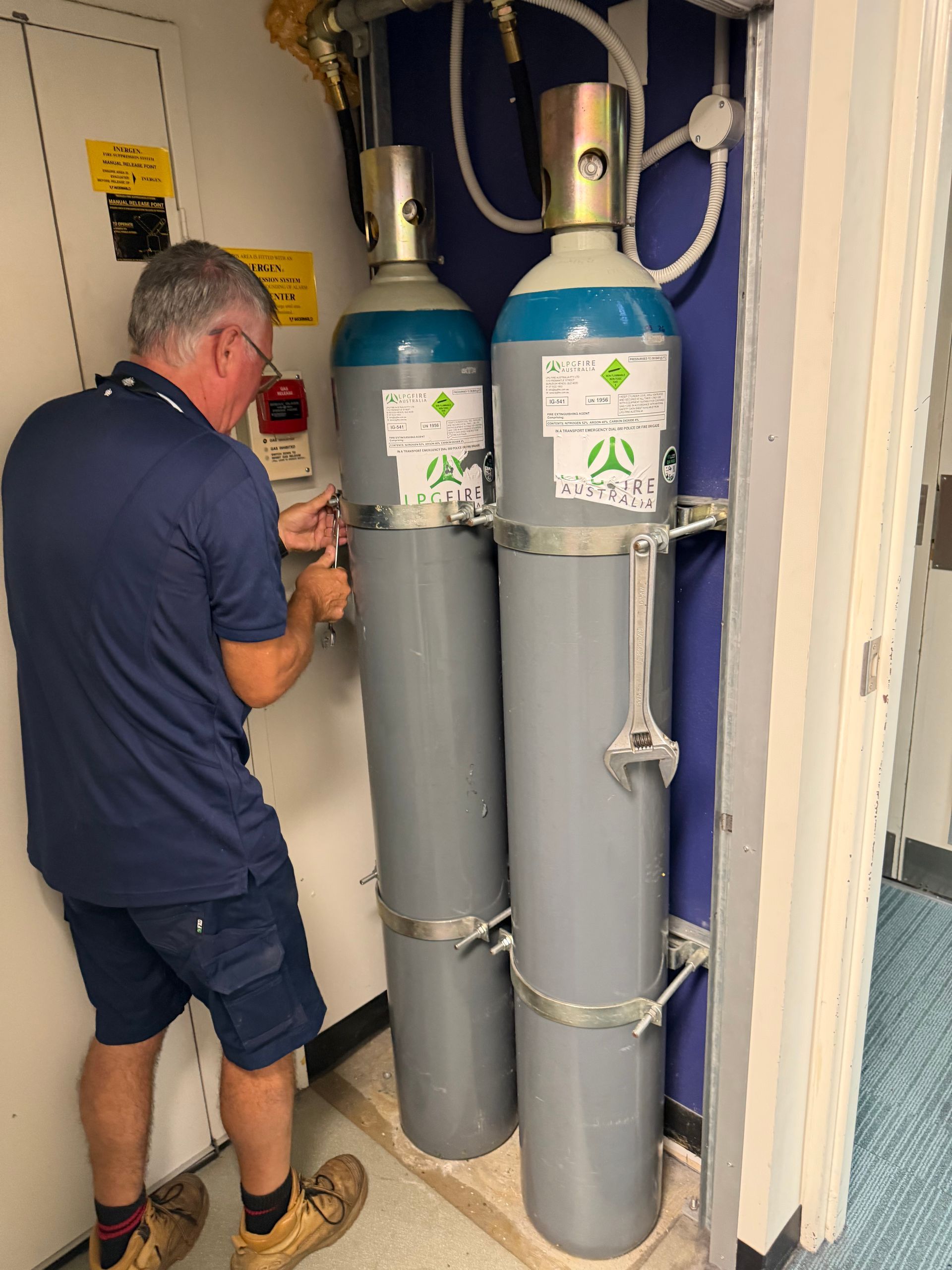 Man Working Beside Two Large Grey Gas Cylinders in a Small Utility Room — Flaming North Fire Protection Pty Ltd in Garbutt, QLD