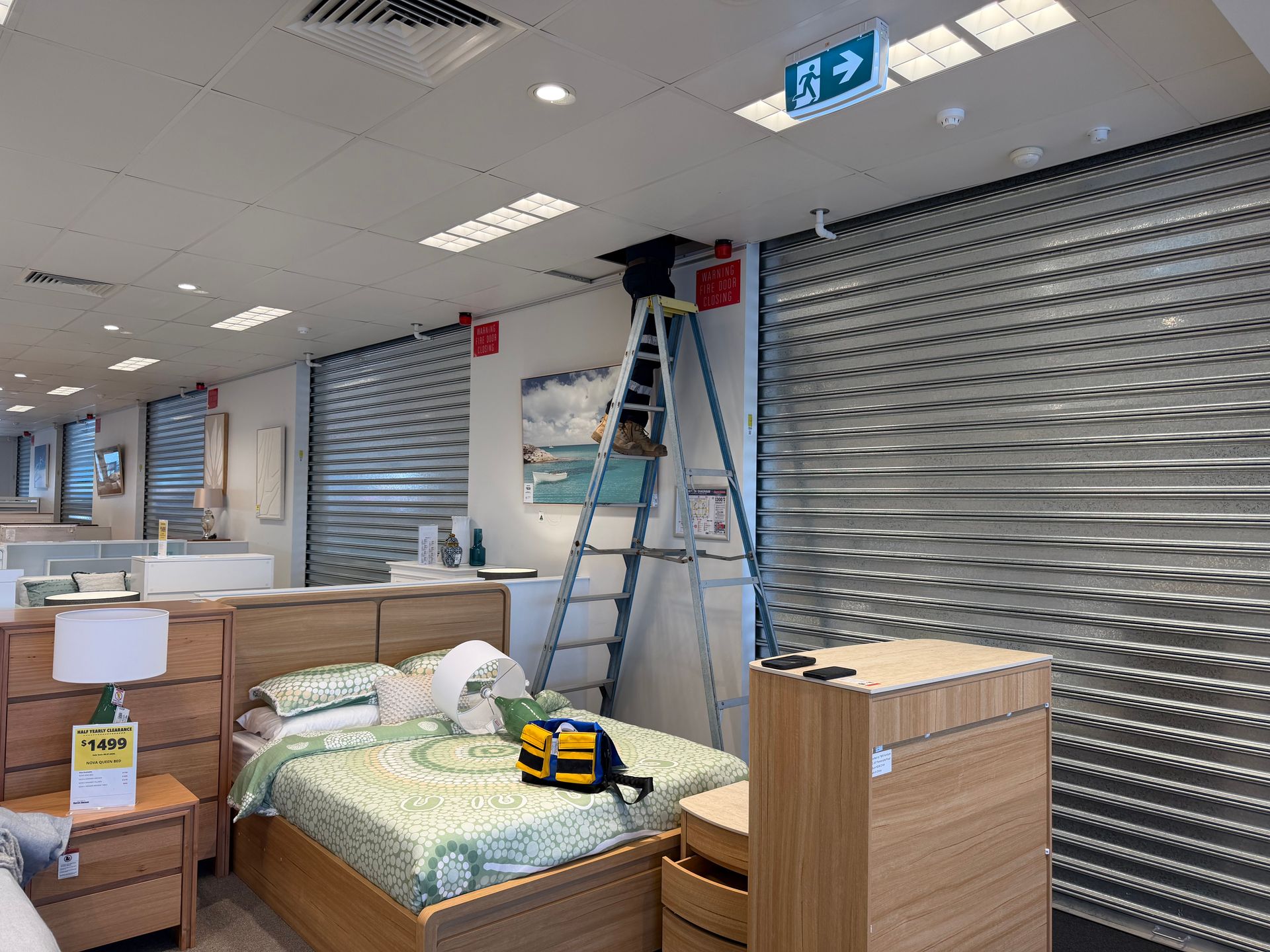 Bed In a Store Display Area With a Ladder, Cabinets, and Closed Metal Shutters Overhead — Flaming North Fire Protection Pty Ltd in Garbutt, QLD