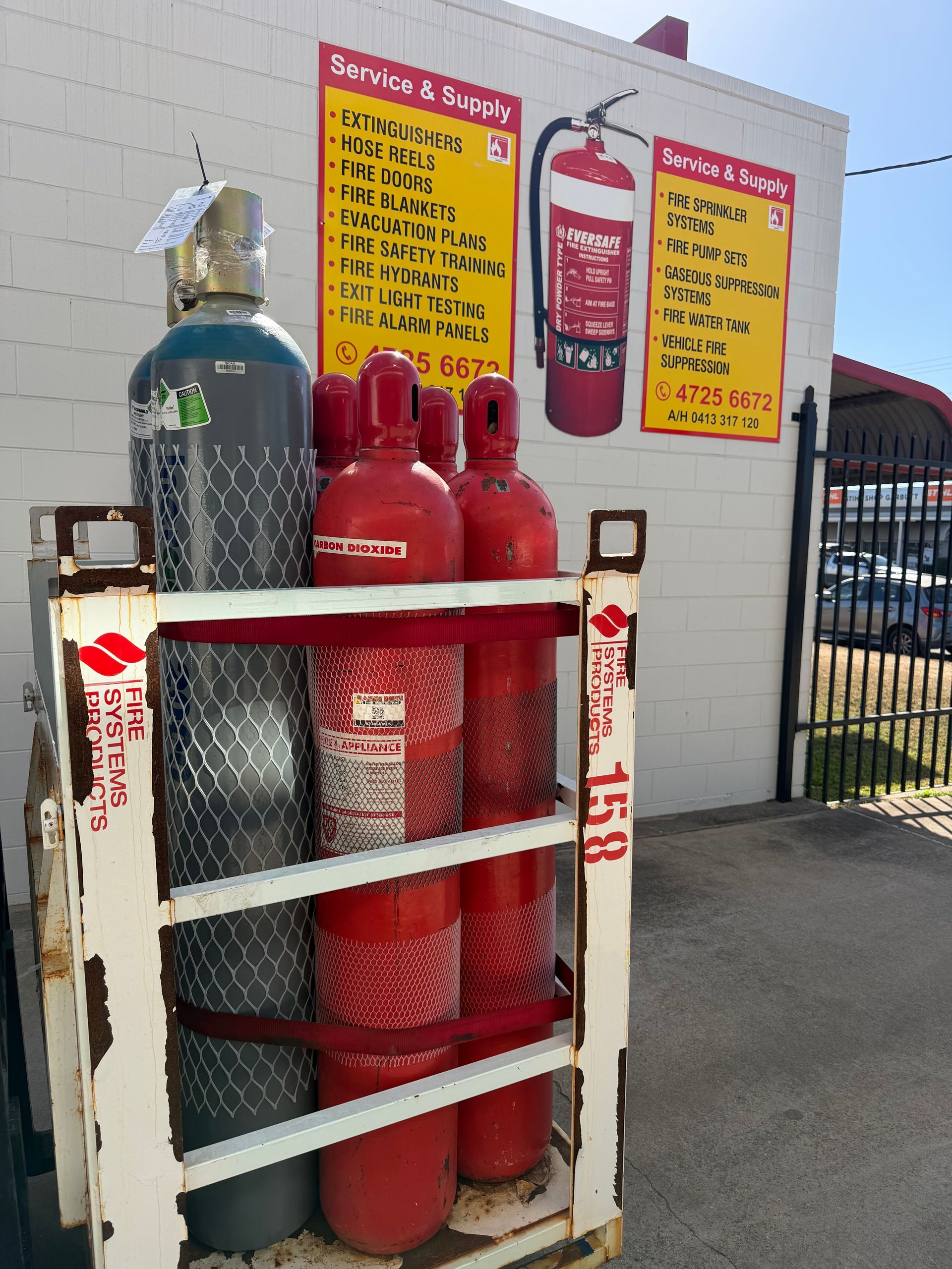Outdoor Gas Cylinder Storage Cage With Red and Green Propane Tanks Beside Safety Signs — Flaming North Fire Protection Pty Ltd in Townsville, QLD