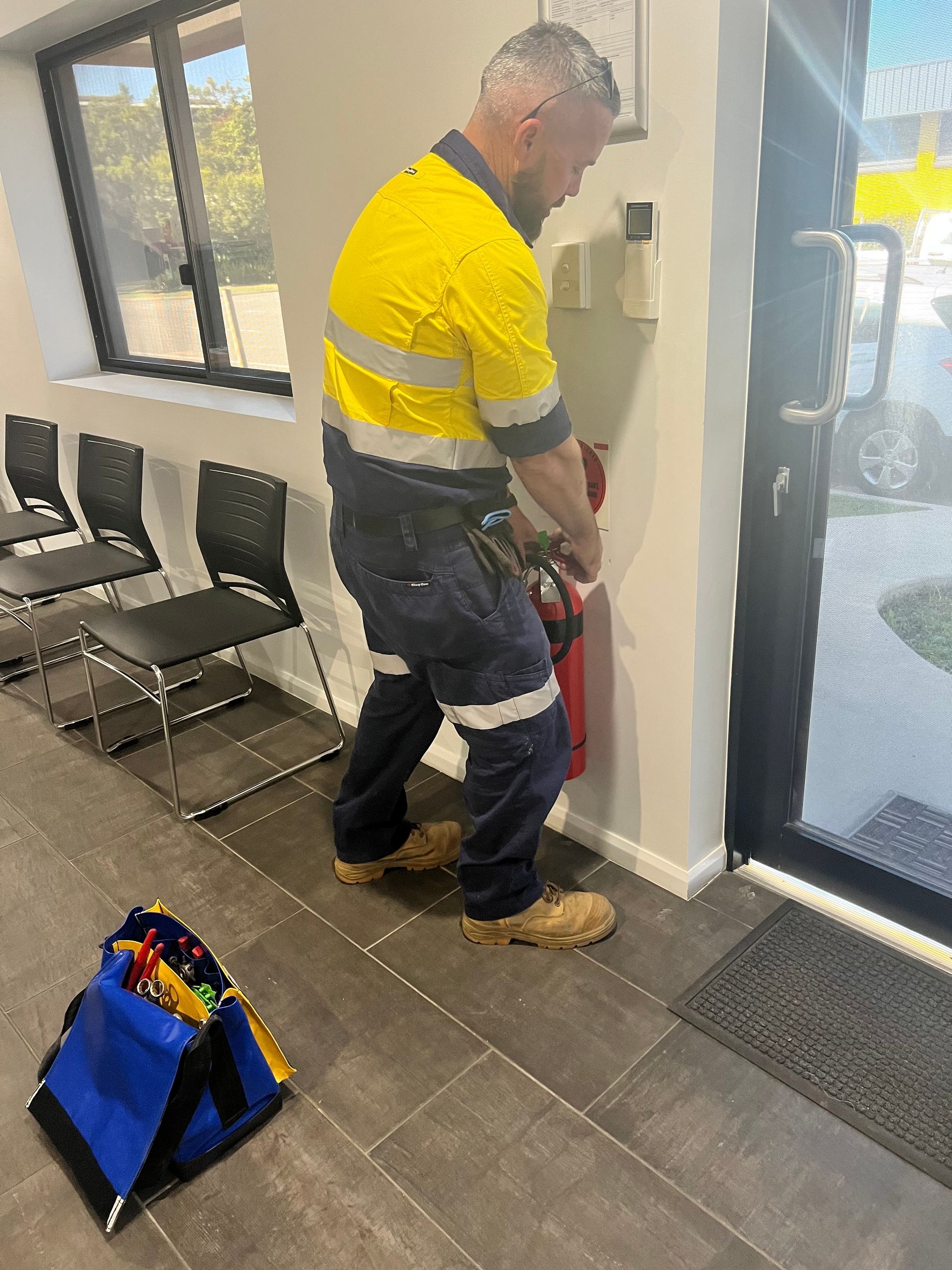 Worker Using a Fire Extinguisher Near a Doorway in a Hallway With Chairs — Flaming North Fire Protection Pty Ltd in Mount Isa, QLD