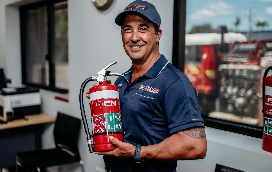 Man In Navy Shirt Holding a Red Fire Extinguisher in an Office Hallway — Flaming North Fire Protection Pty Ltd in Garbutt, QLD