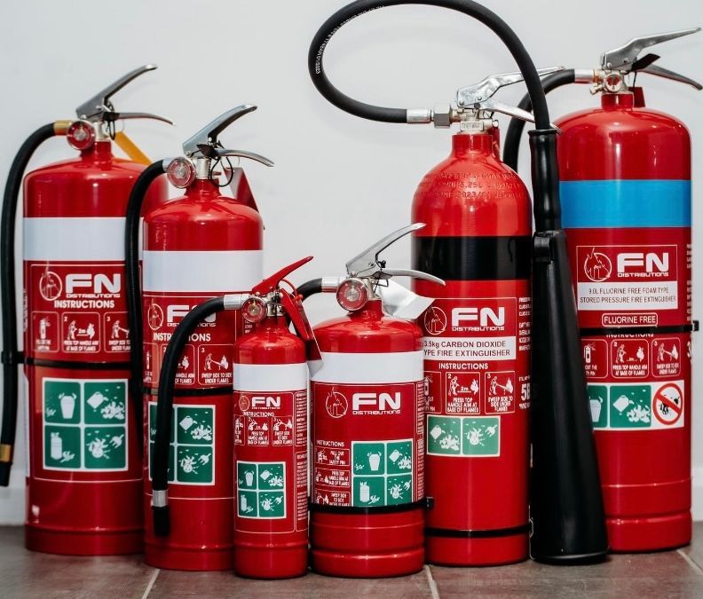 Red Fire Extinguishers of Various Sizes Lined Up on a White Background With a Hose Attached to One Large Unit — Flaming North Fire Protection Pty Ltd in Garbutt, QLD