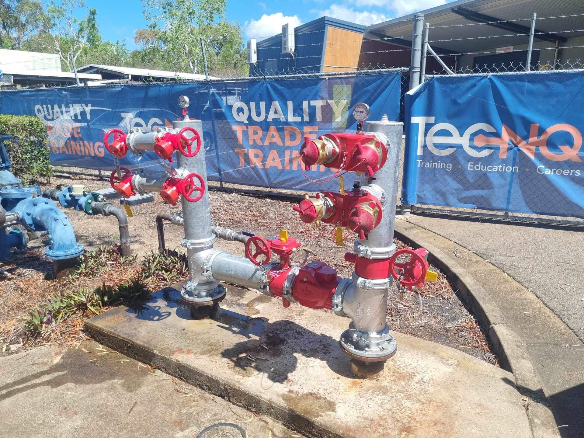 Red Industrial Valves and Pipes in Front of a Blue Construction Site Banner — Flaming North Fire Protection Pty Ltd in Garbutt, QLD